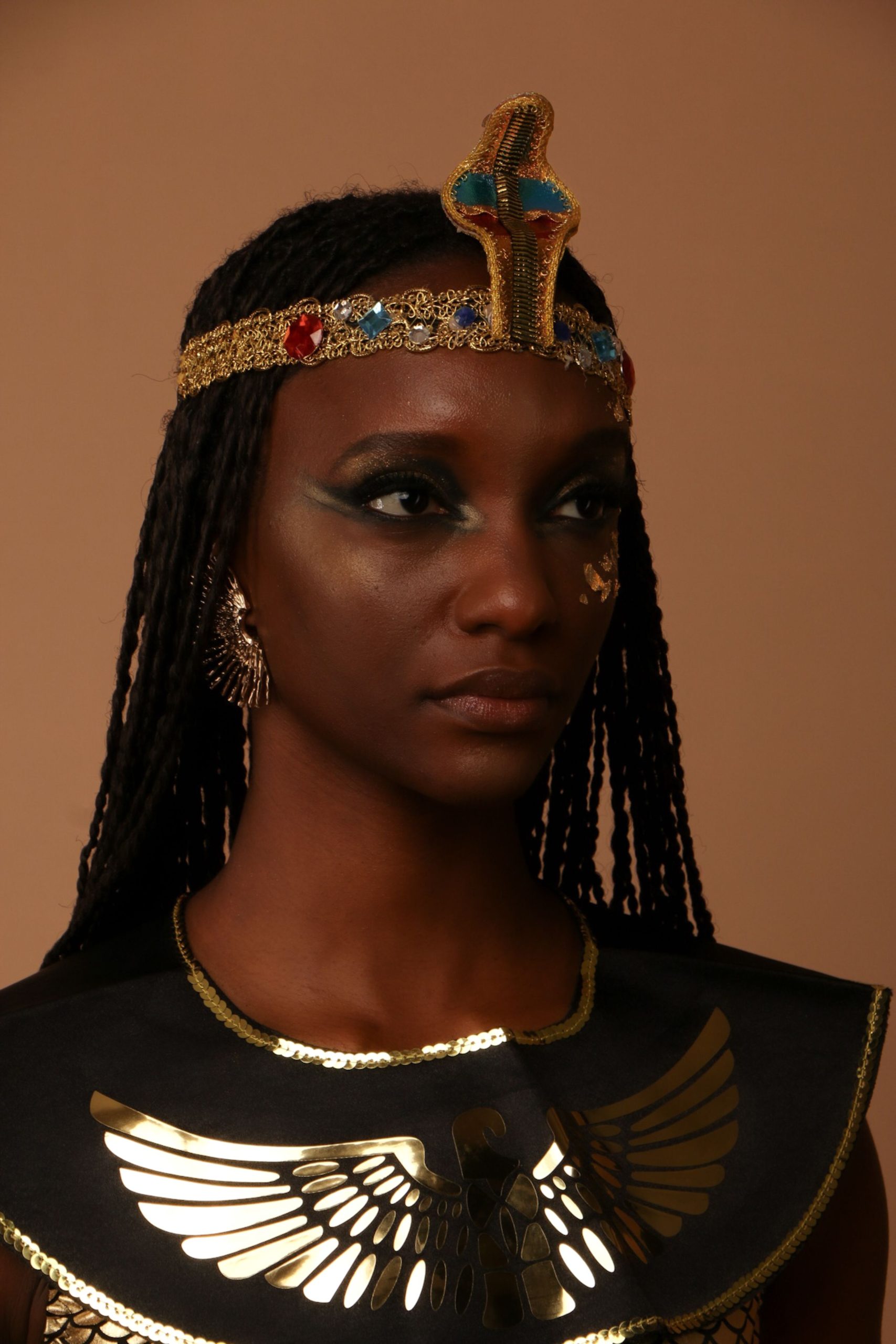 A woman dressed in an Egyptian costume poses confidently against a neutral background.