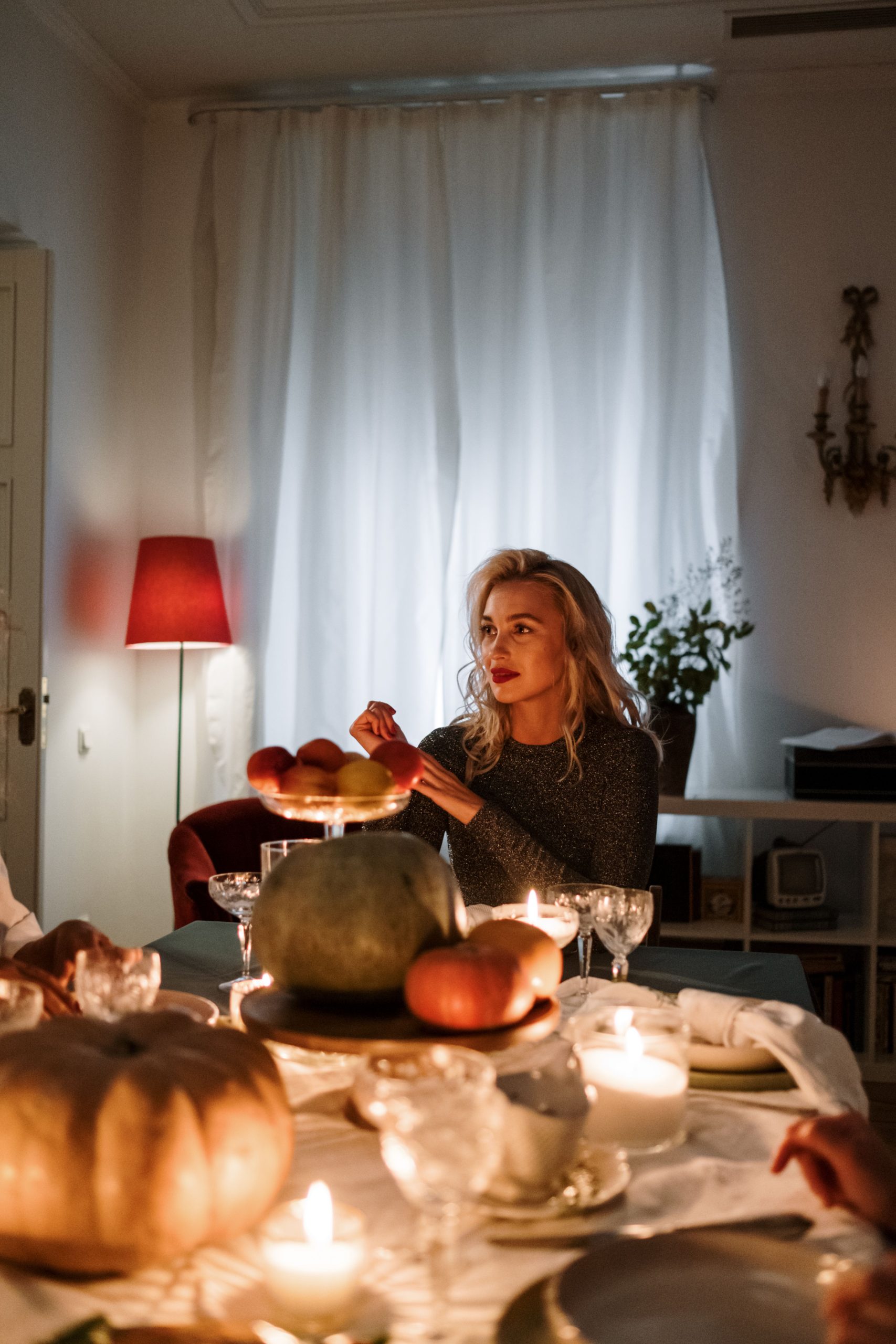 A woman enjoying a candlelit dinner with pumpkins and wine glasses, creating a warm, cozy atmosphere.