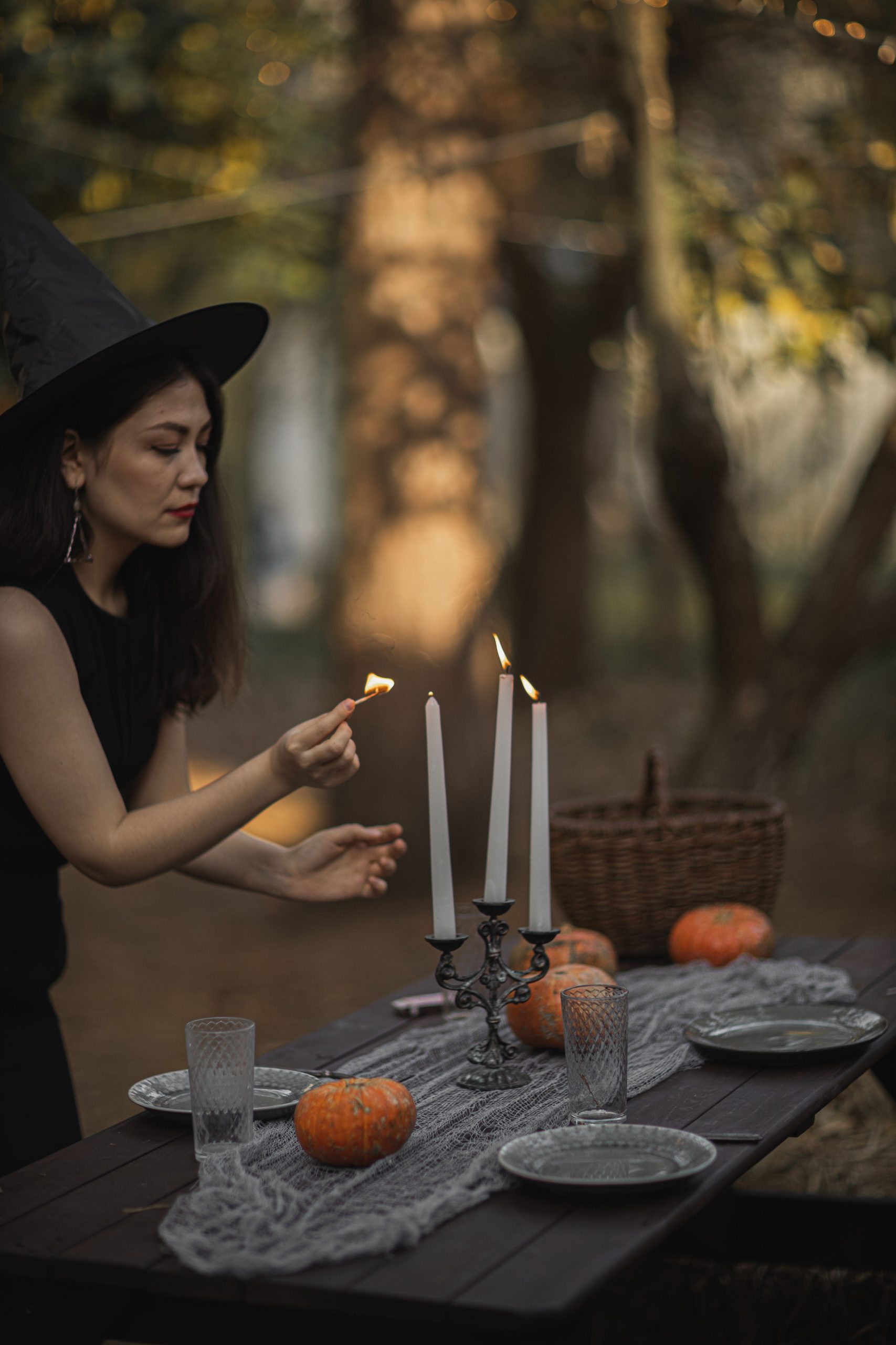 A woman in a witch costume lights candles on a pumpkin-decorated table during autumn.