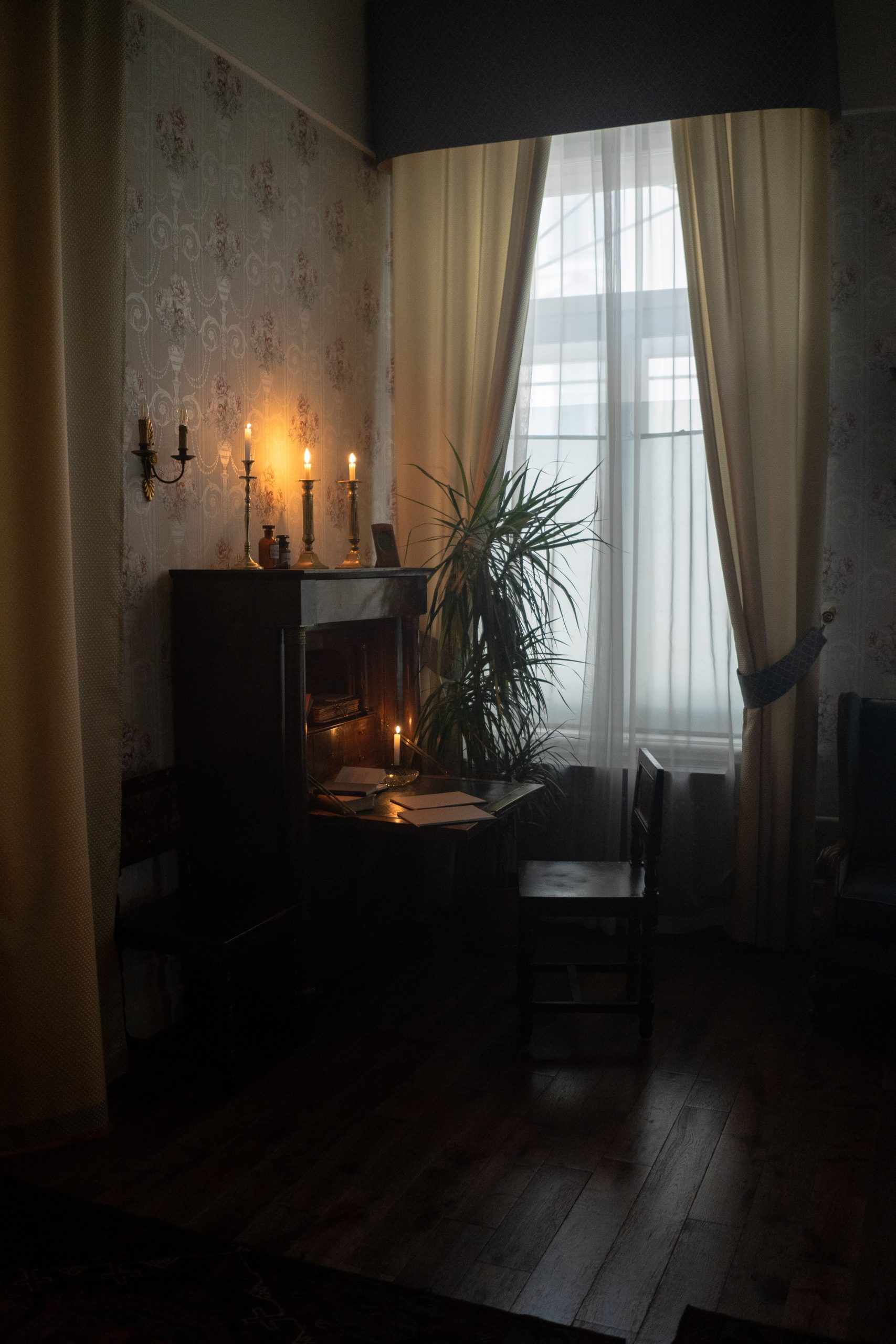 An intimate, vintage-style room with candles lighting a small desk by a window with soft curtains.