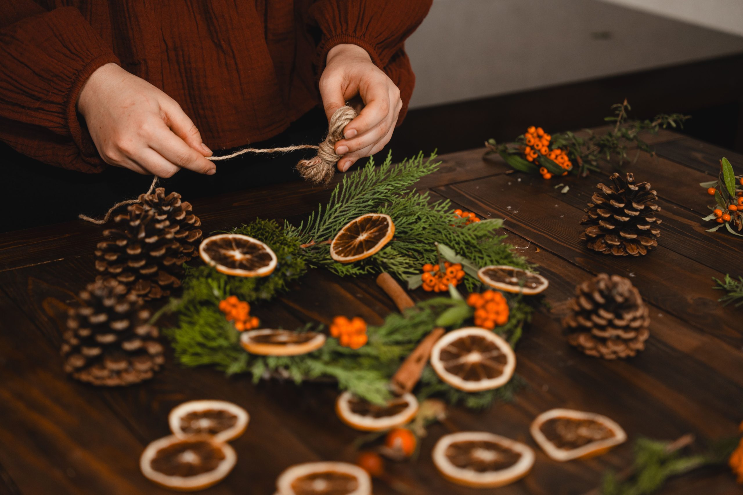 Artisan crafting a holiday wreath with natural pine cones and dried oranges.