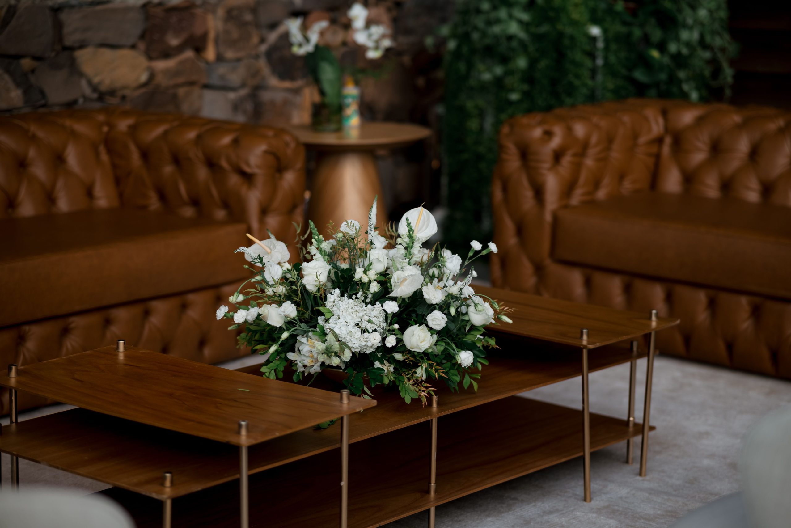 Beautiful white flower arrangement on wooden coffee table in cozy living room with leather sofas.