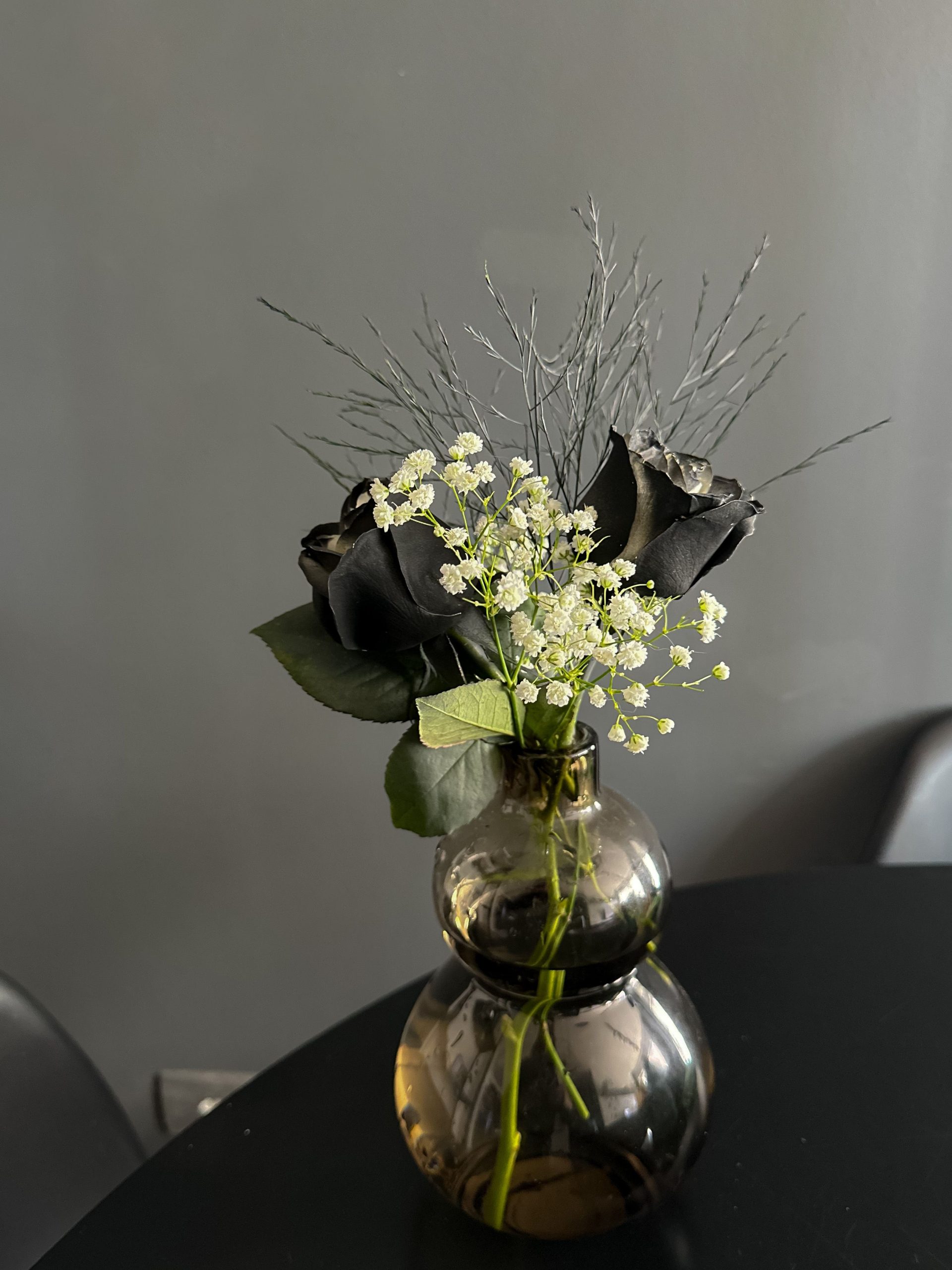 Black roses and delicate flowers in a vase on a dark table, perfect for modern decor themes.