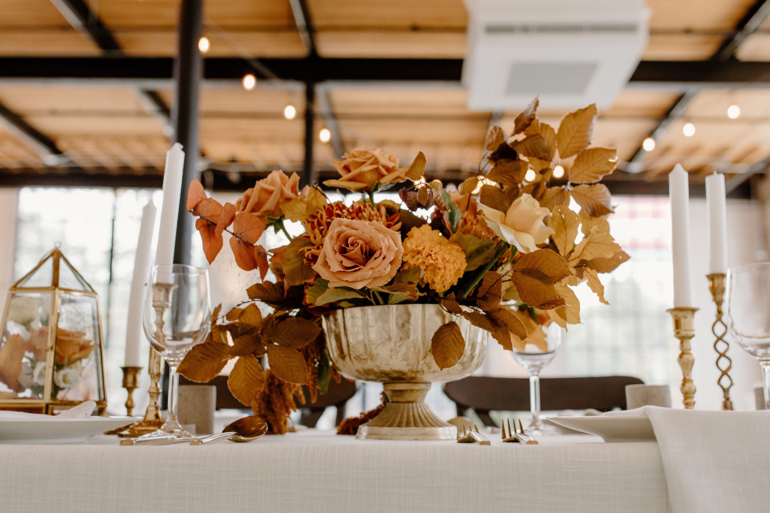 Bouquet of flowers with foliage placed on table with wineglasses and candles during festive event in modern restaurant with decorations
