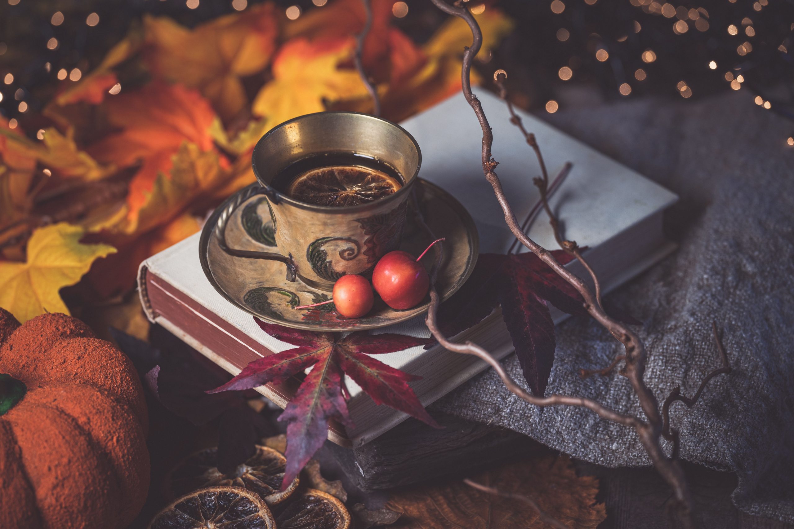 Charming autumn still life featuring a cup of tea with books, pumpkin, and maple leaves.