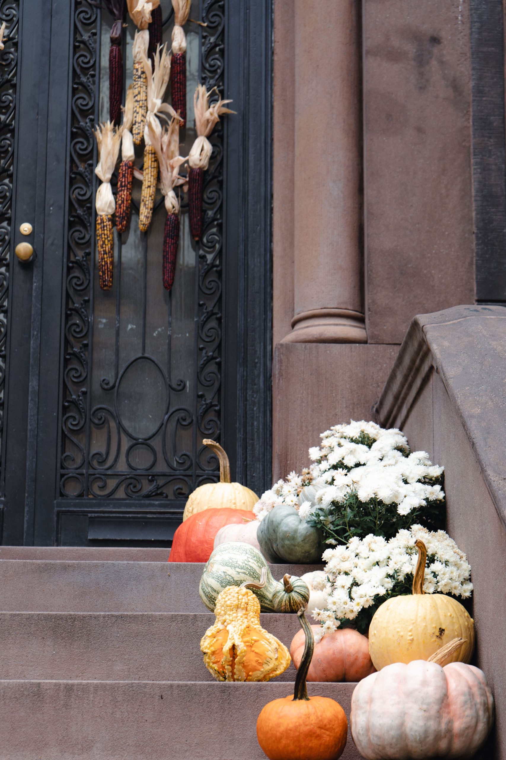 Charming fall decorations with pumpkins and corn adorn brownstone steps, creating a festive autumn atmosphere.