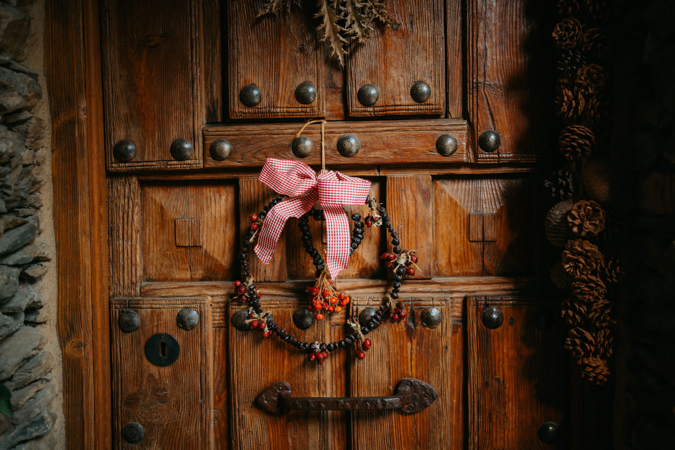 Charming old wooden door adorned with a handmade berry wreath and a red checkered bow.
