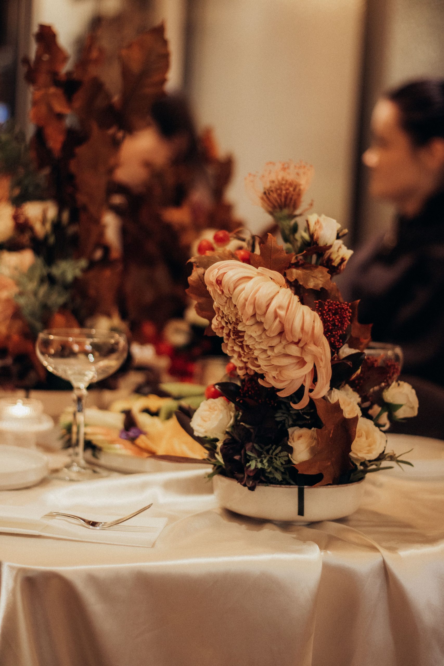 Chic floral centerpiece with autumn foliage on an elegant dining table setting.