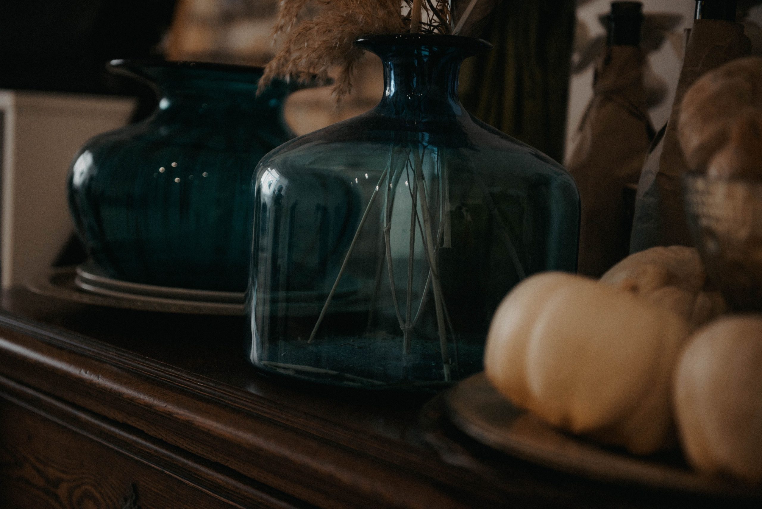 Close-up of blue glass vases, dried plants, and white pumpkins on a wooden dresser, creating a rustic decor setting.