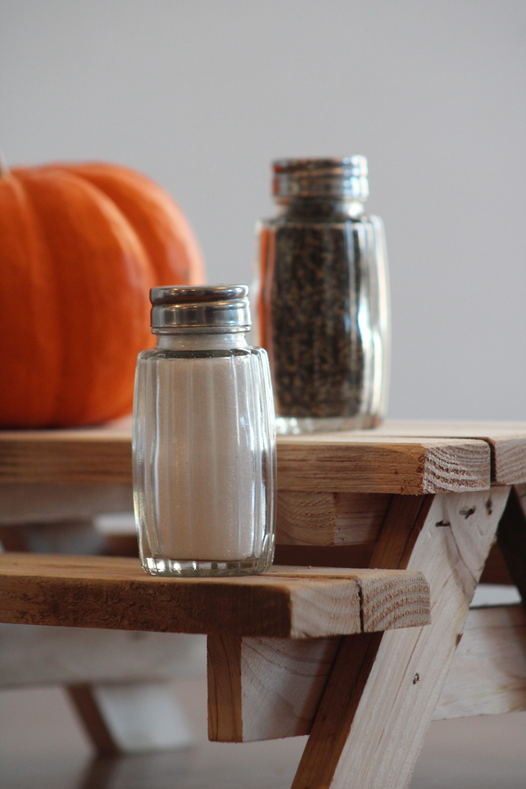 Close-up of salt and pepper shakers with pumpkin on wooden table.