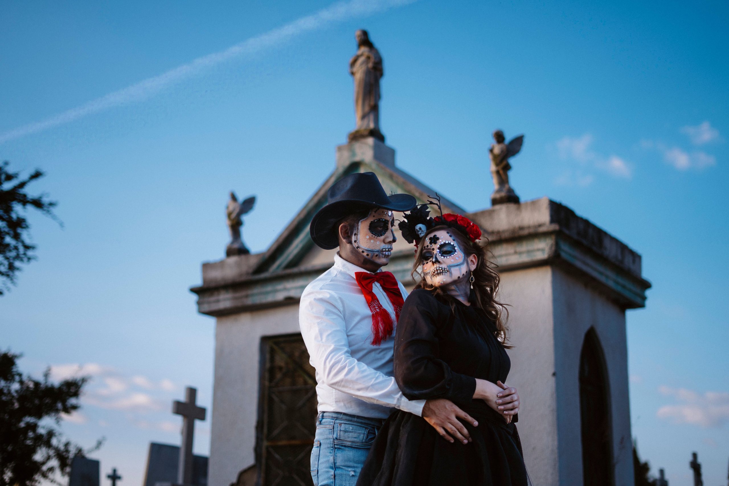Couple dressed in Day of the Dead costumes in a cemetery setting at sunset.