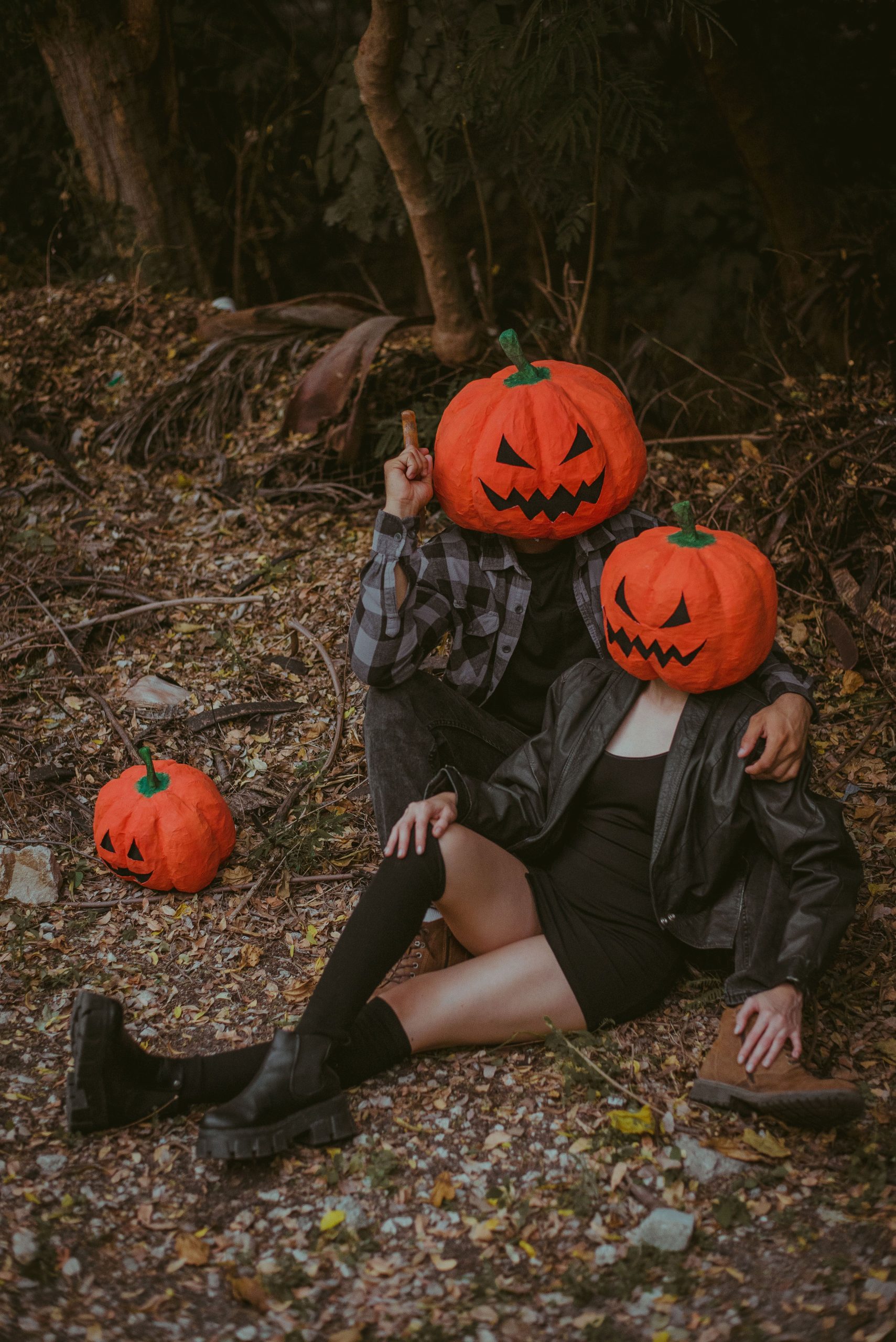 Couple with pumpkin heads posing outdoors in a Halloween-themed concept photo.