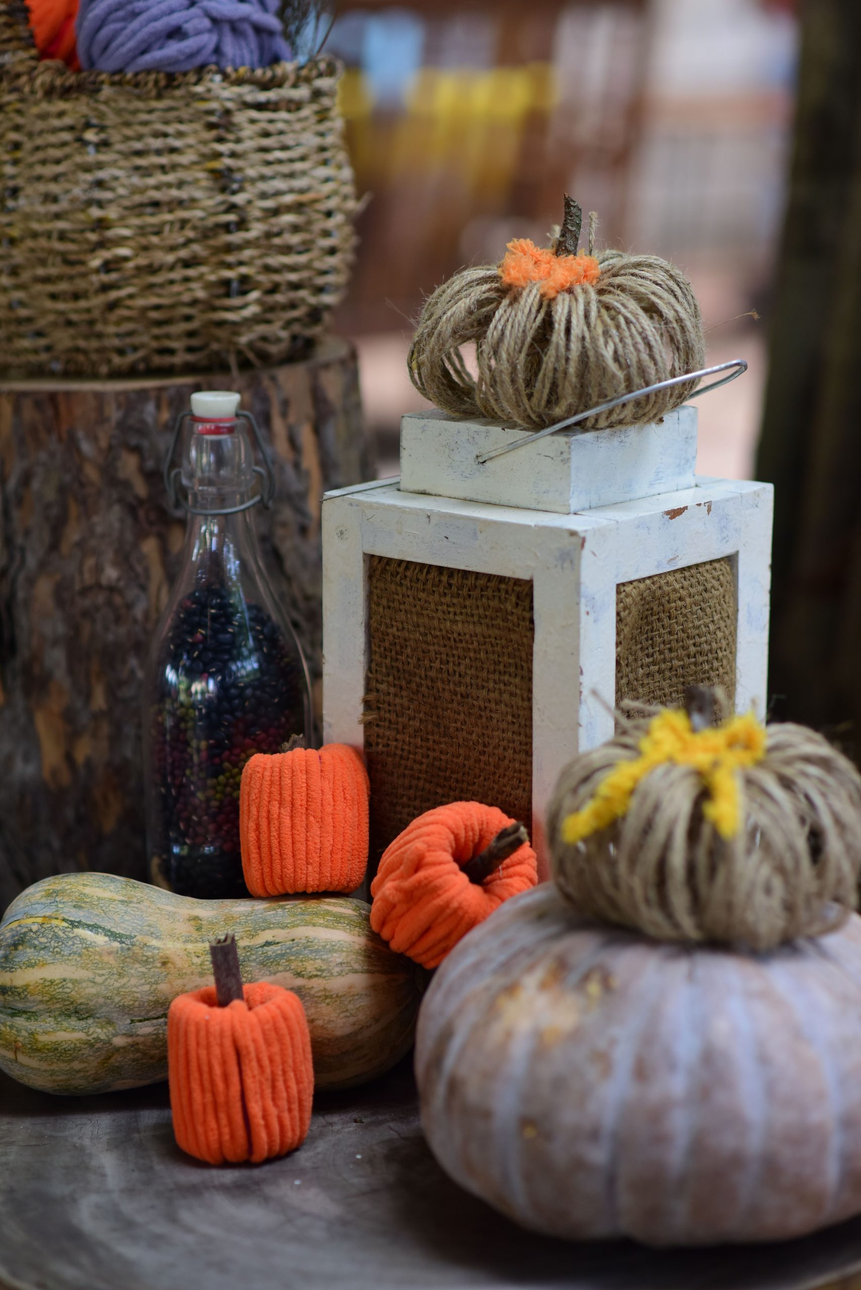Cozy autumn display featuring handmade yarn pumpkins, a rustic lantern, and dried gourds.