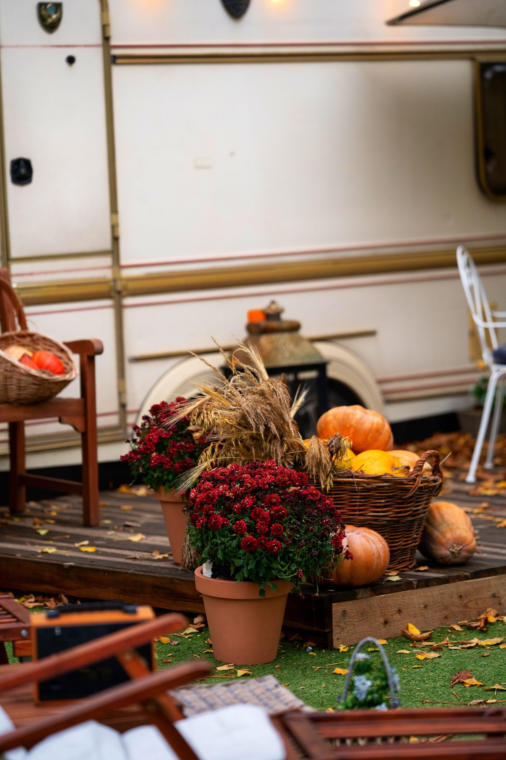 Cozy autumn scene with pumpkins, red flowers, and baskets on a wooden porch outdoors.