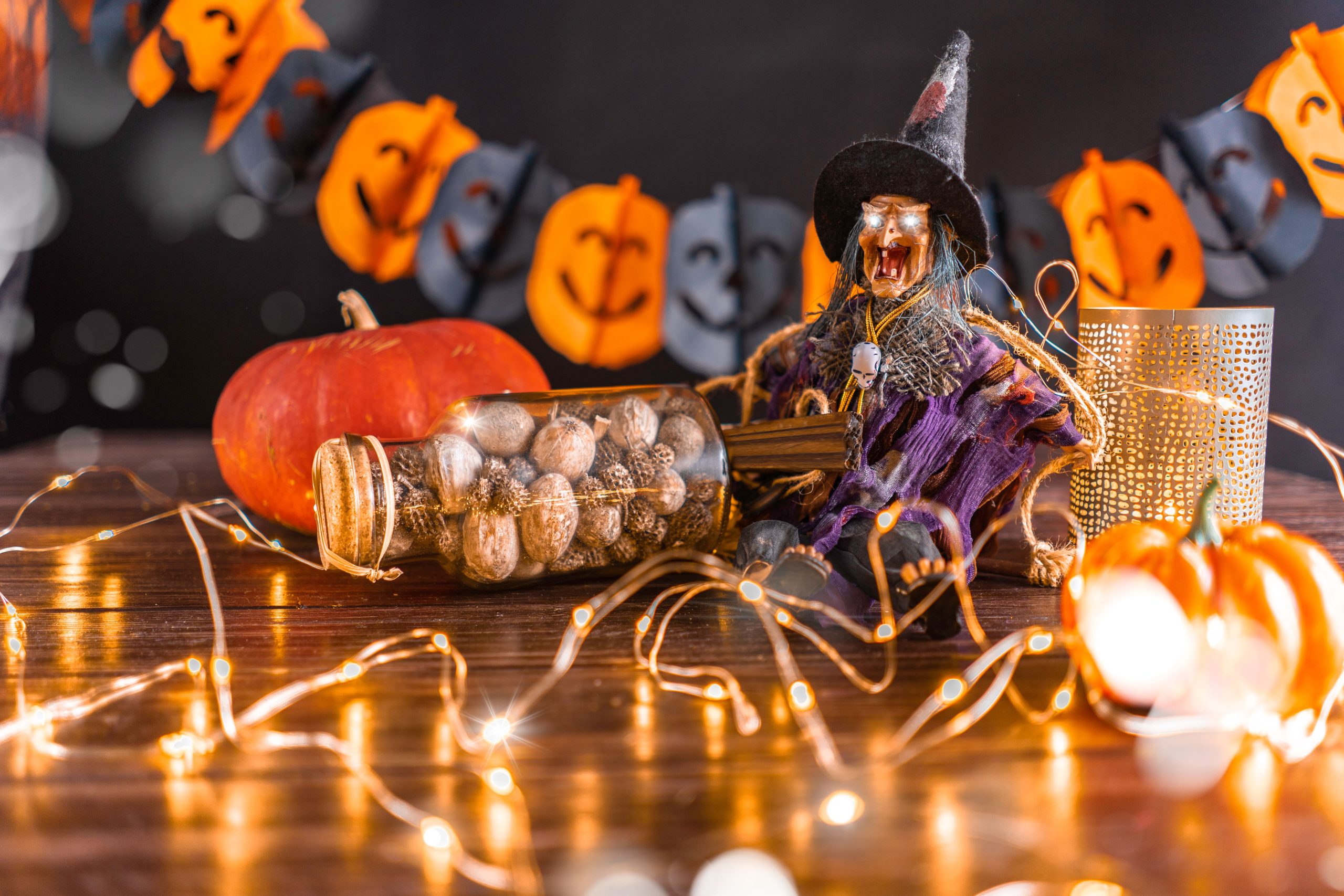 Cozy Halloween table with witch figurine, pumpkins, and string lights.