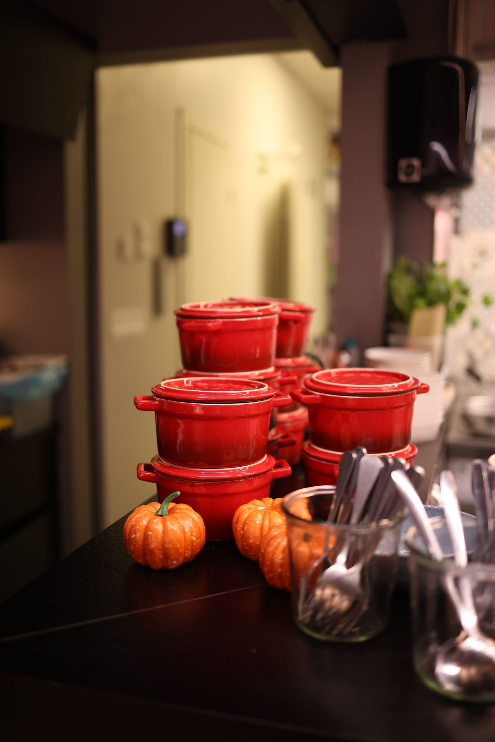Cozy kitchen scene with stacked red ceramic pots and mini pumpkins on a countertop.
