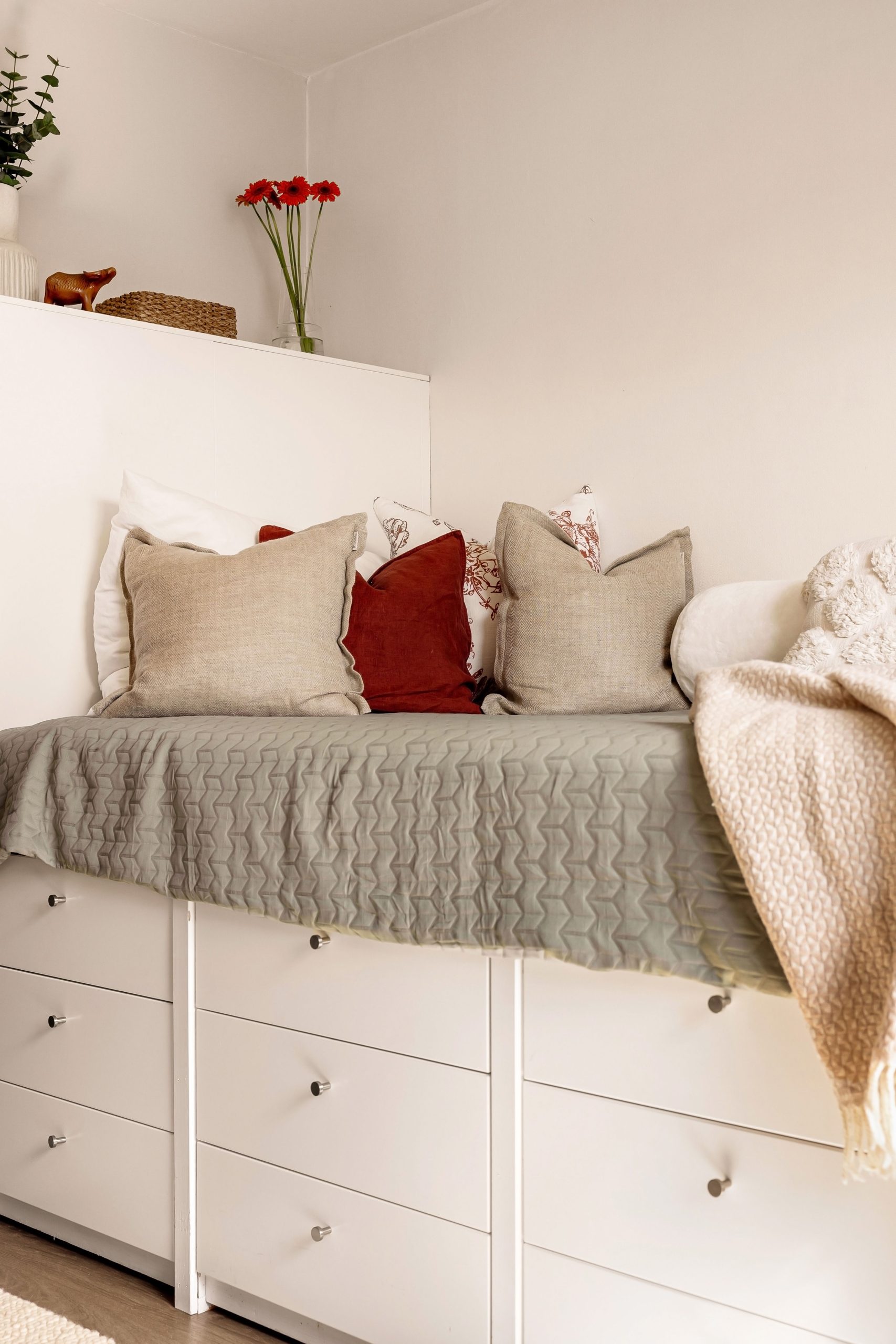 Cozy minimalist bedroom setup with pillows, floral decor, and warm lighting.