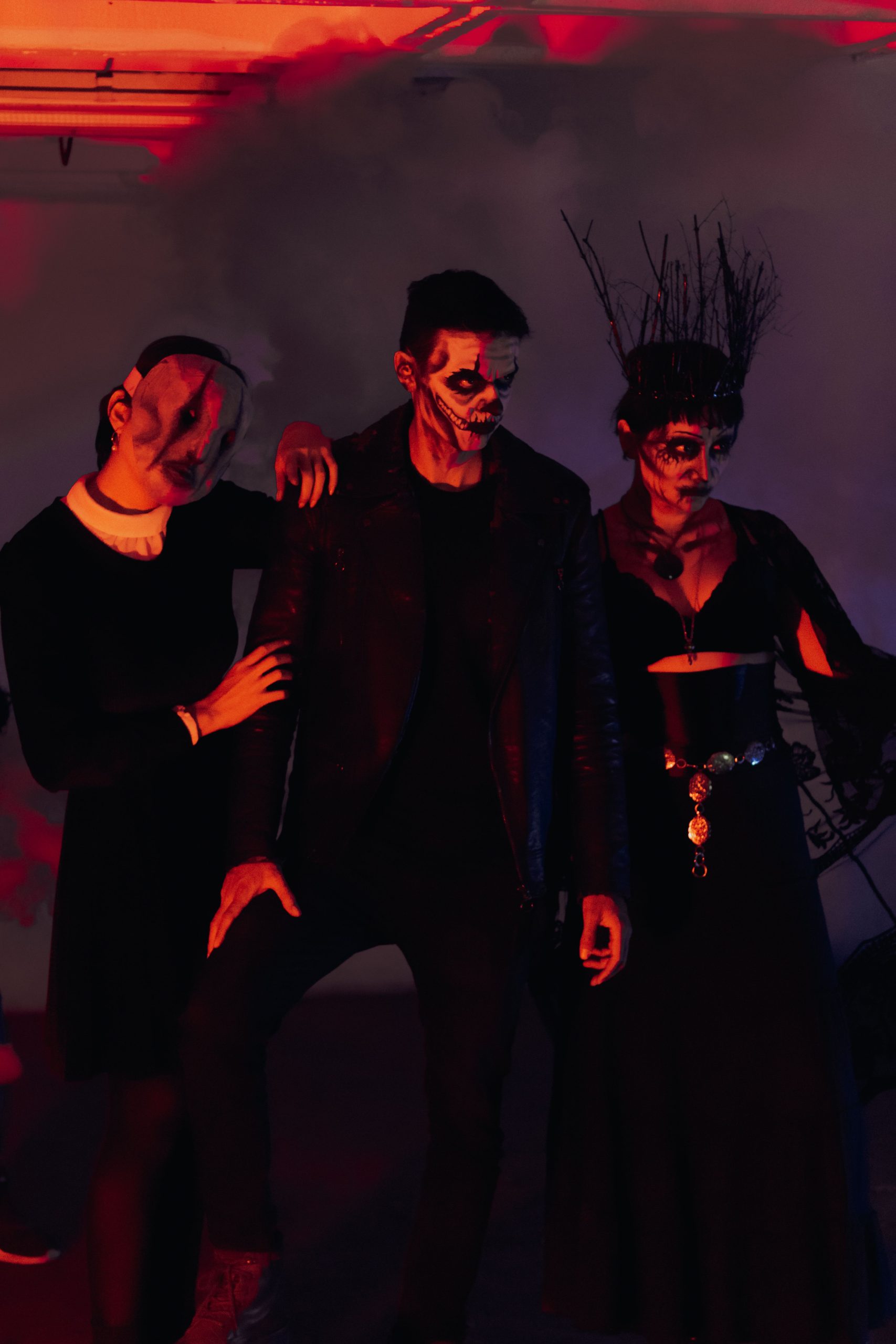 Dark and moody portrait of three adults in Halloween costumes, with dramatic lighting.