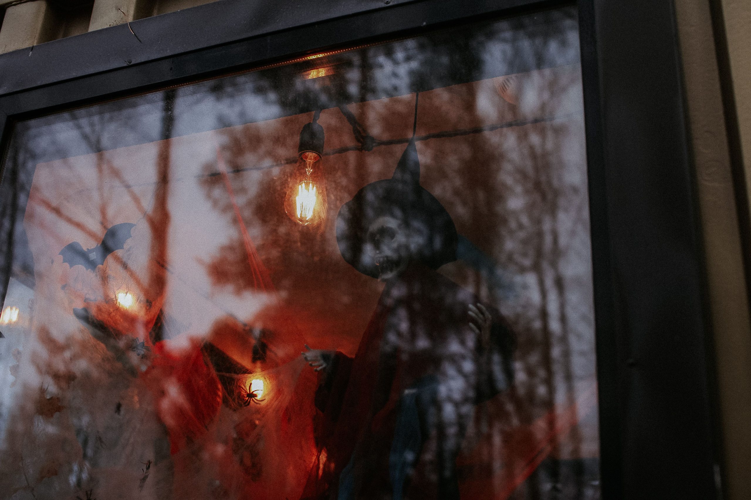 Eerie Halloween decor featuring a witch and bats in a glass window with reflections.
