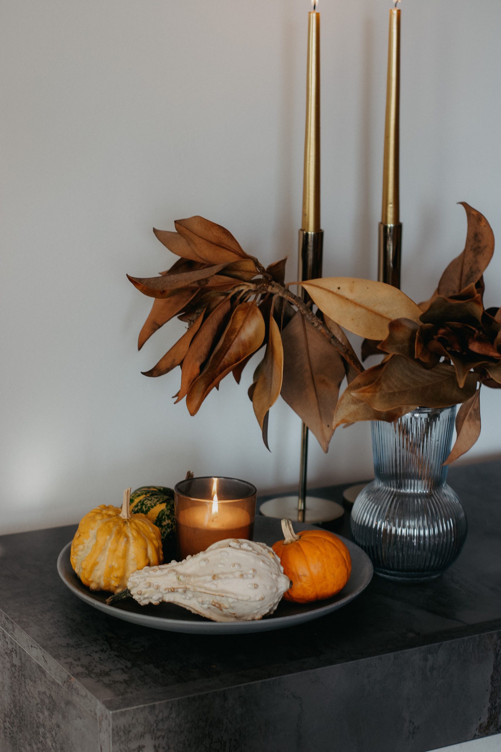 Elegant autumn arrangement with pumpkins, candle, and leaves in a vase.