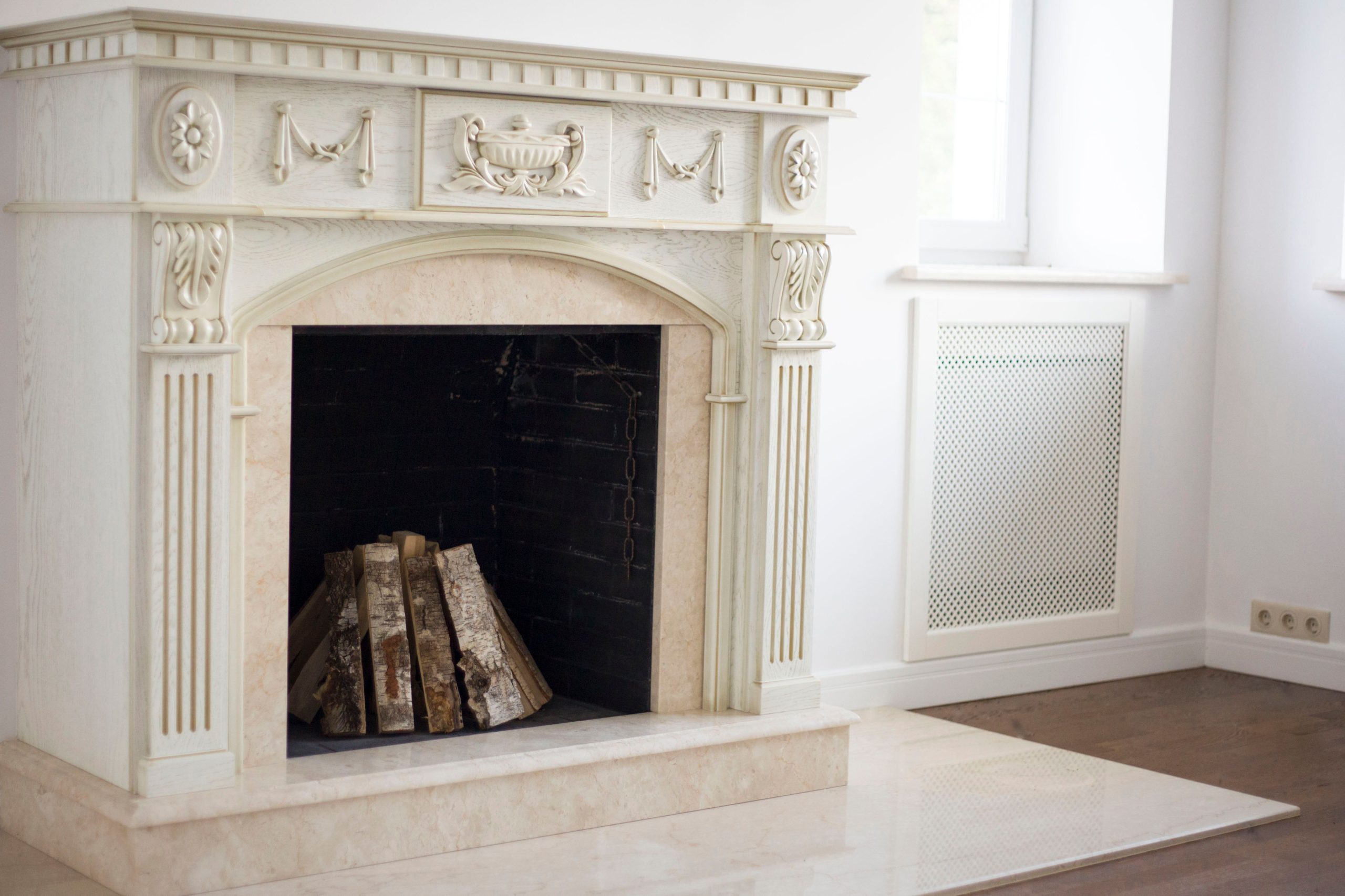 Elegant classic fireplace with firewood set in a bright, indoor home setting, surrounded by white walls and detailed craftsmanship.
