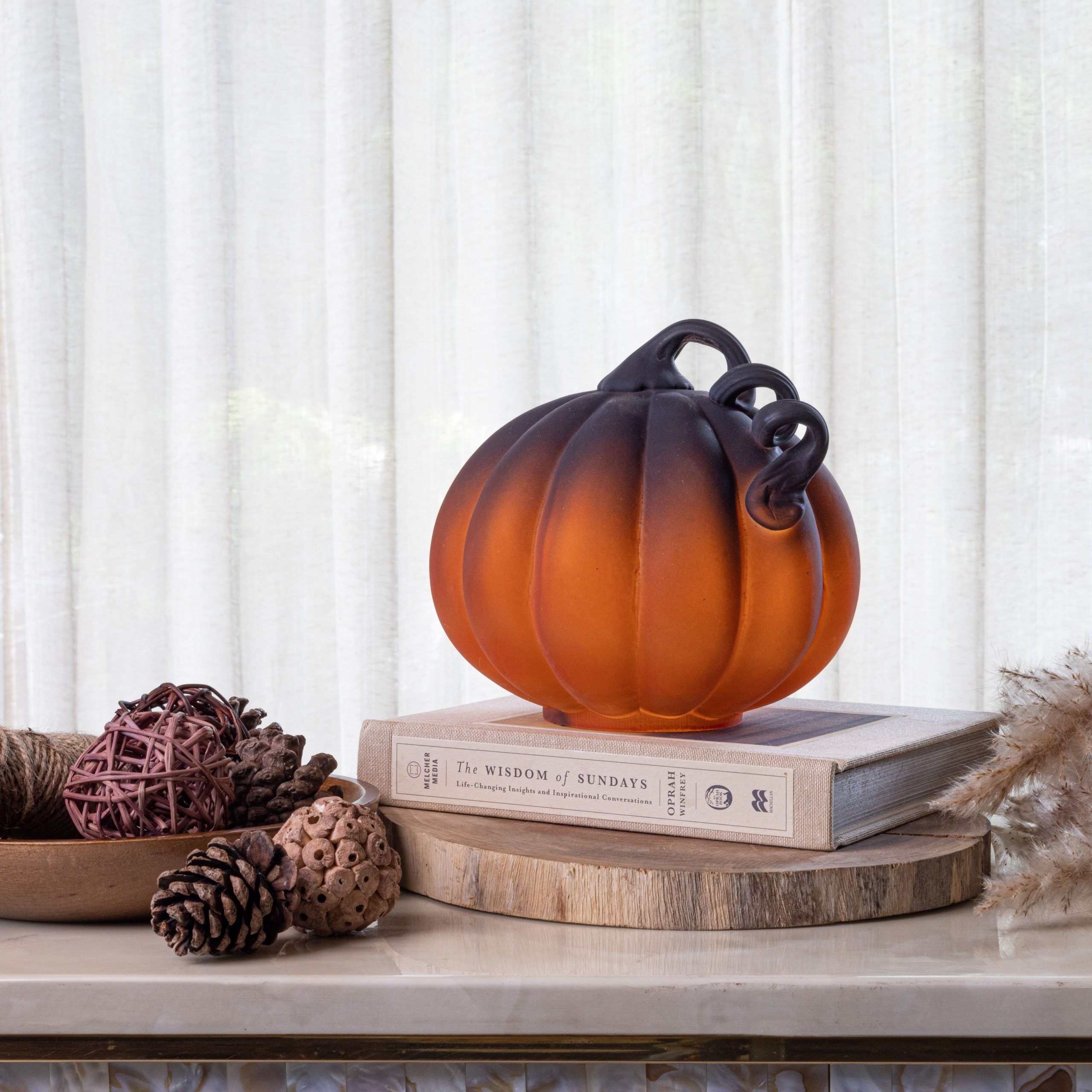 Elegant glass pumpkin centerpiece on books with pinecones and fall decor indoors.