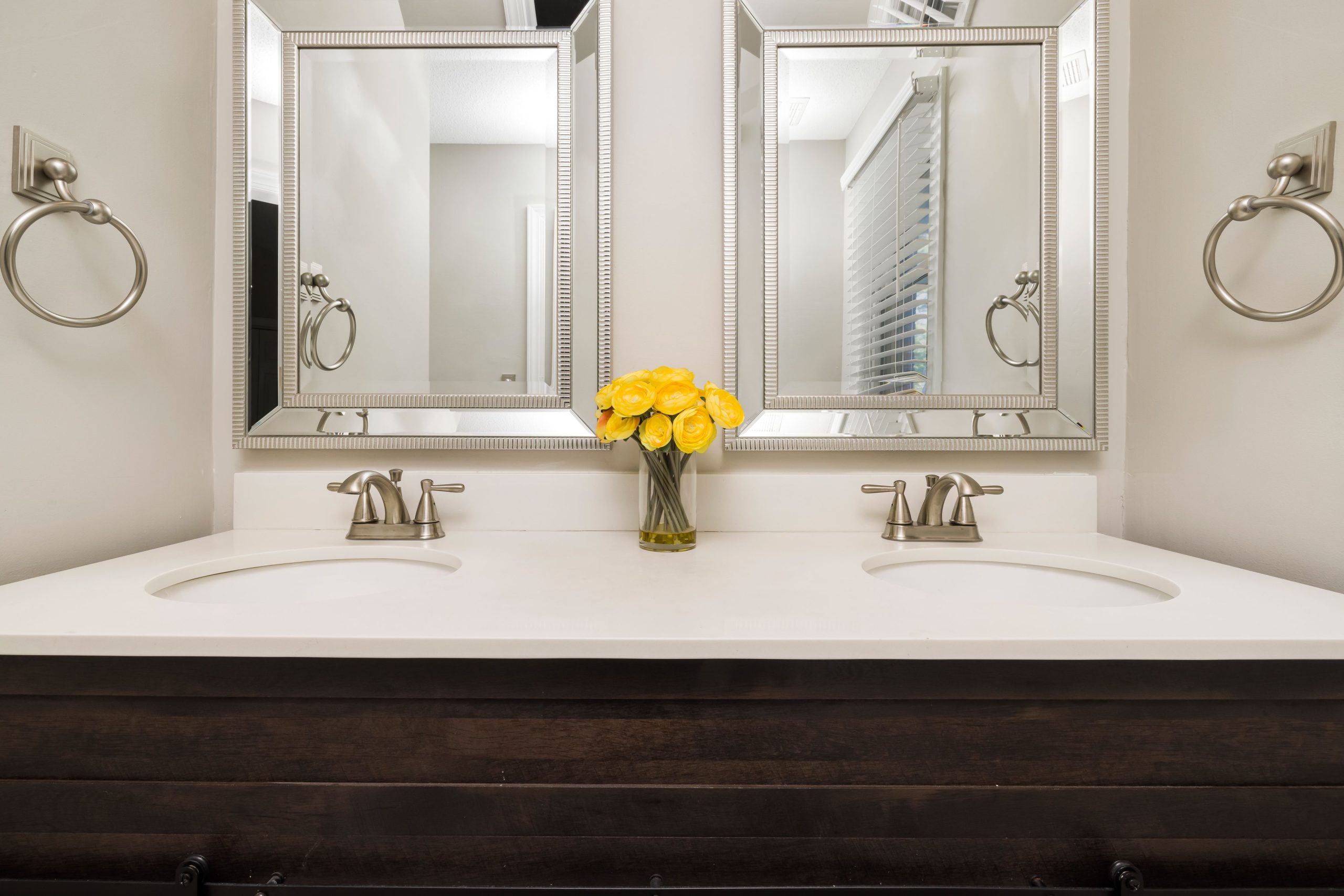 Elegant modern bathroom with twin mirrors, stylish faucets, and a touch of luxury with yellow flowers.