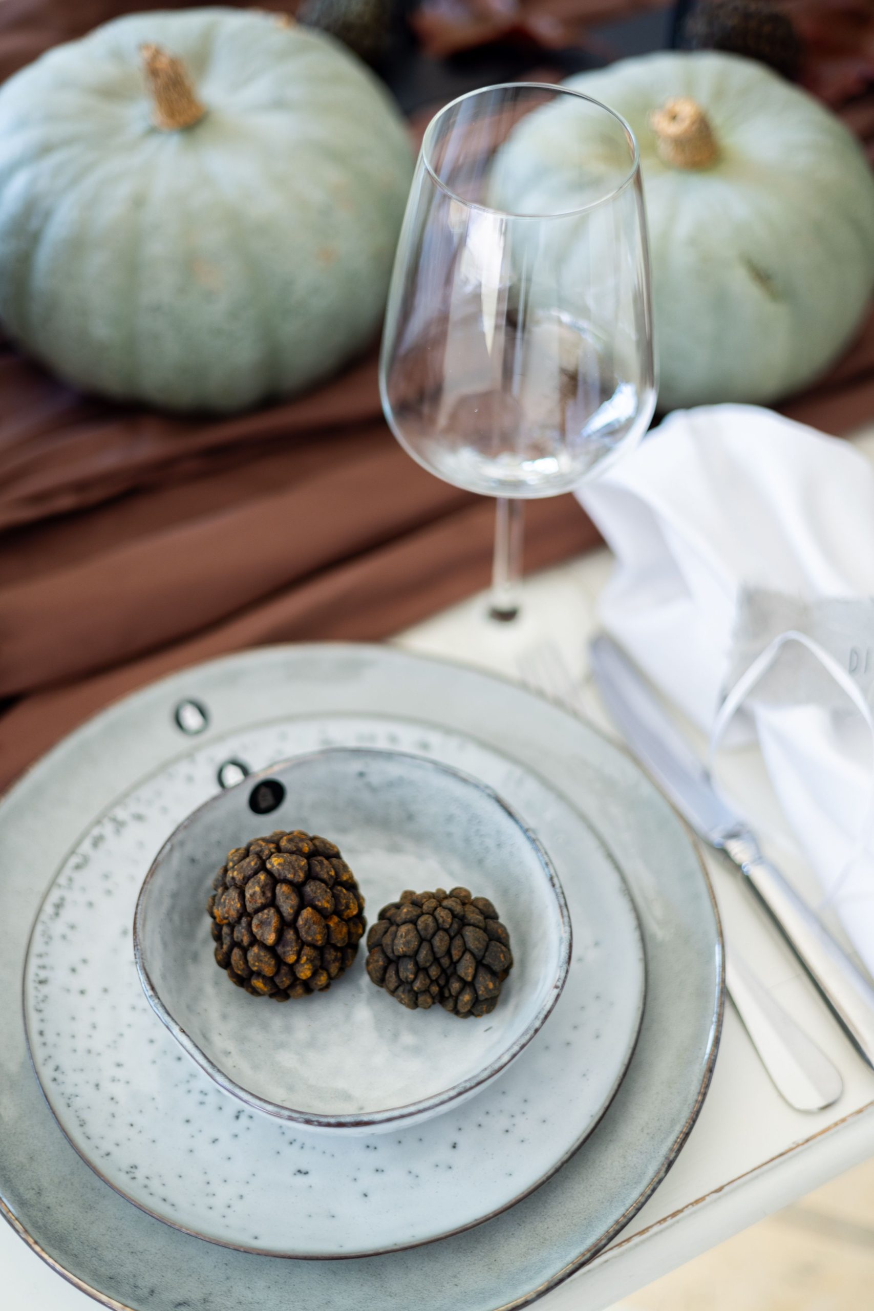 Elegant table setup featuring truffles, pumpkins, and a wineglass.