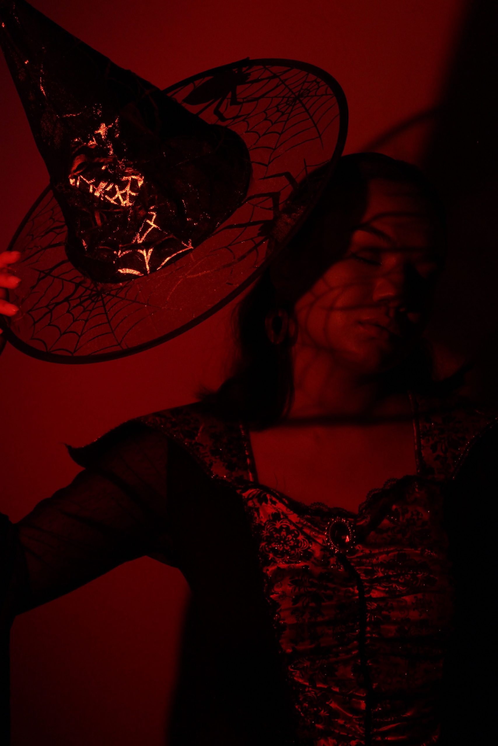Enchanting portrait of a woman in a witch costume under dramatic red lighting.