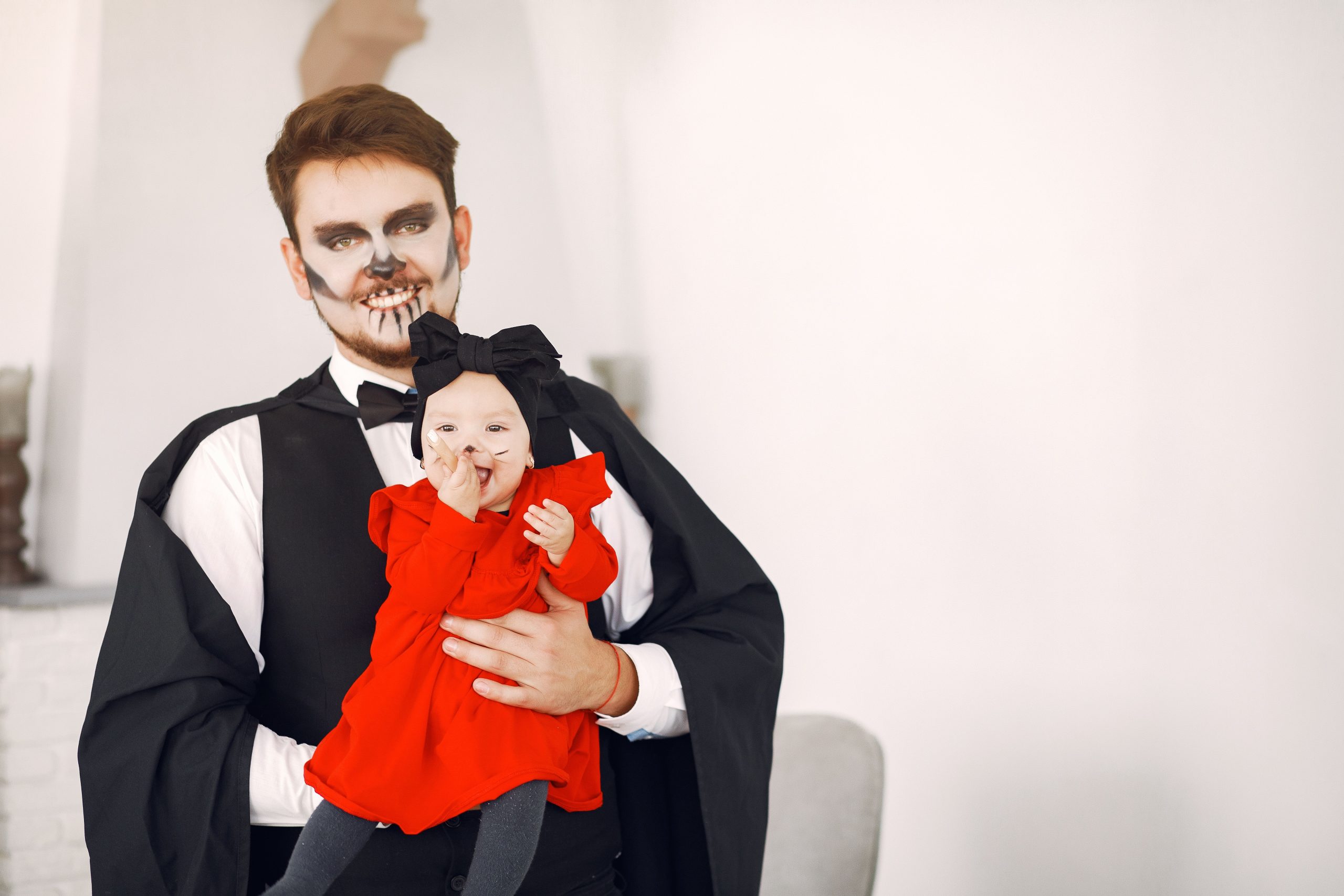 Father and baby in costumes celebrating Halloween indoors with festive face paint.