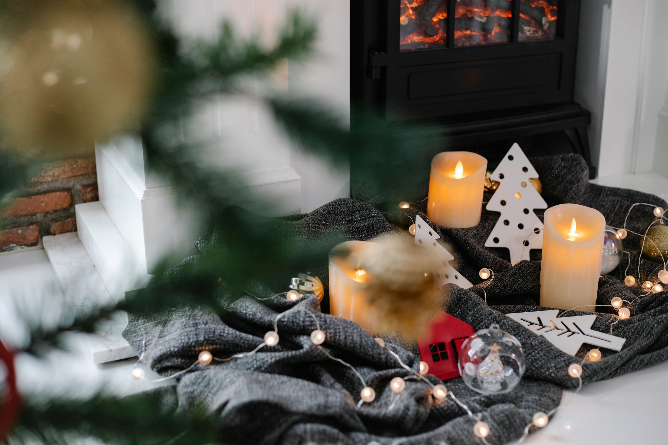 Festive decorations with candles and garland near fireplace in room with Christmas tree