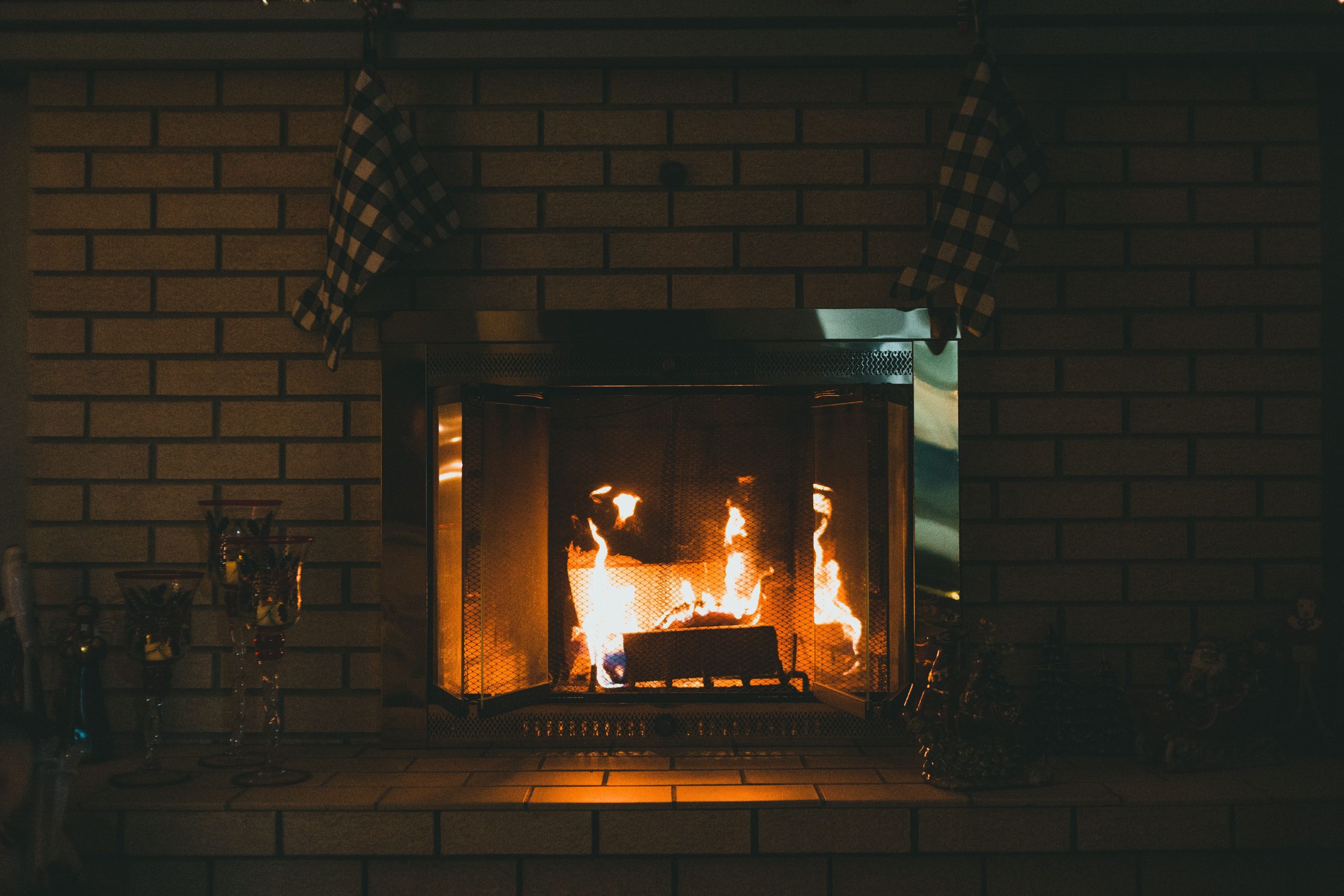 Fireplace with shiny flaming fire between retro glass candle holders and statuettes against brick wall in house