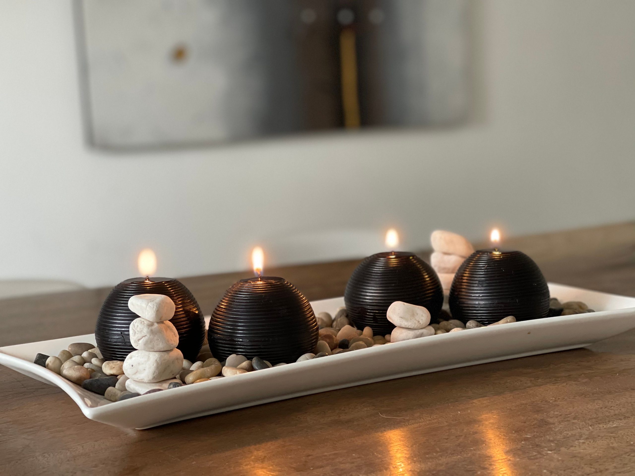 Four lit black candles on a tray surrounded by pebbles create a serene ambiance.