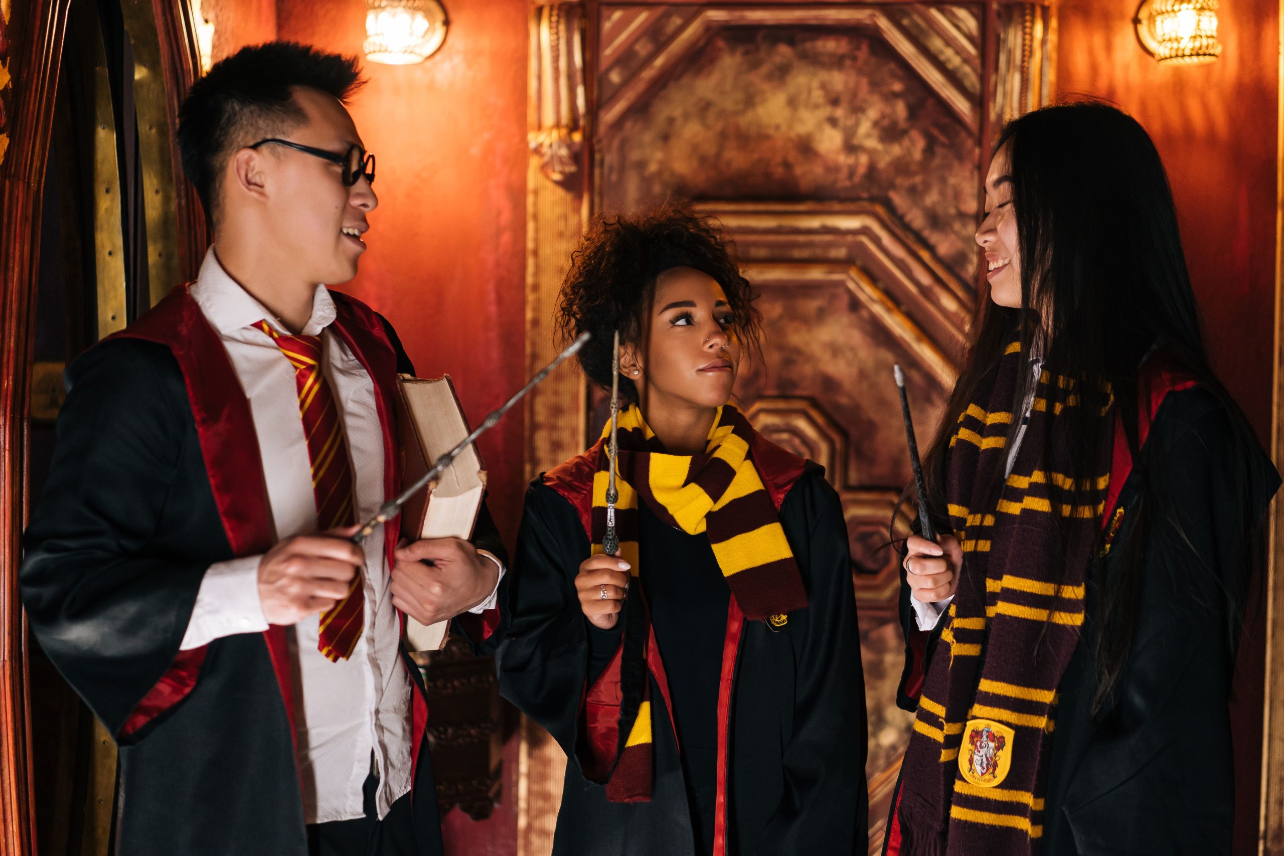 Friends dressed in magical costumes with wands and scarves sharing a moment indoors.