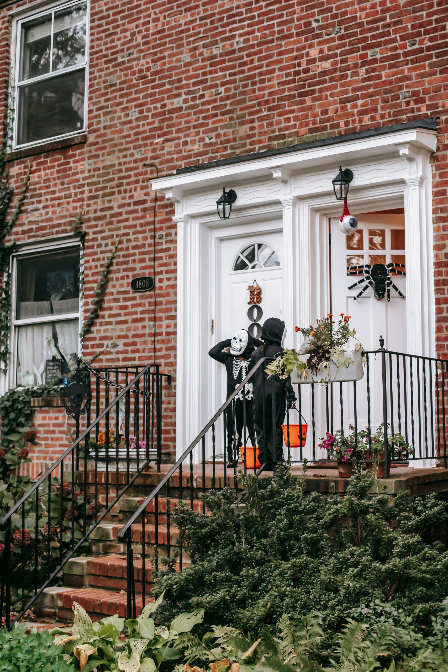 Full body of unrecognizable children in Halloween black skeleton costumes with masks standing near house entrance with orange buckets
