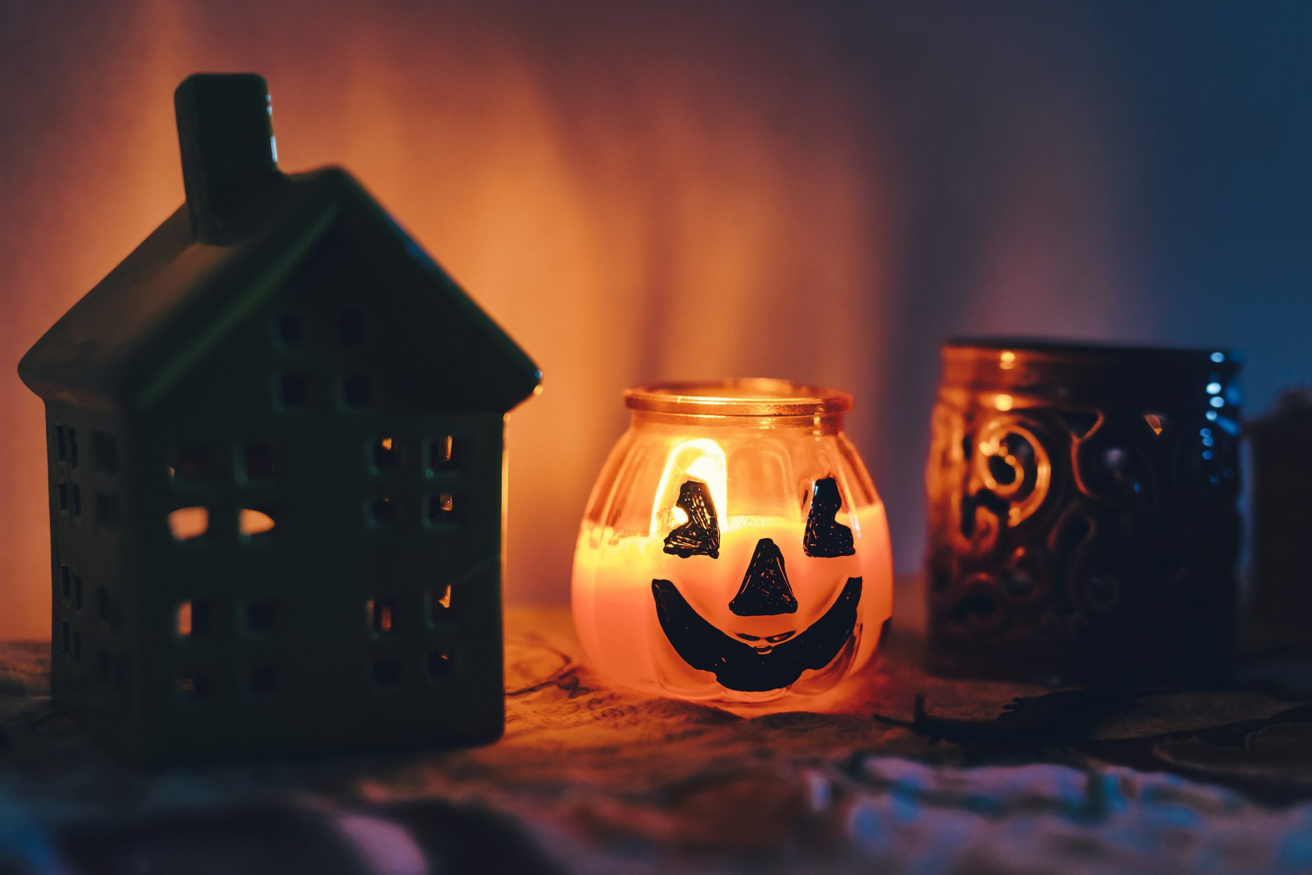 Halloween candle next to candle holders on a bench. Moody morning light on wall.