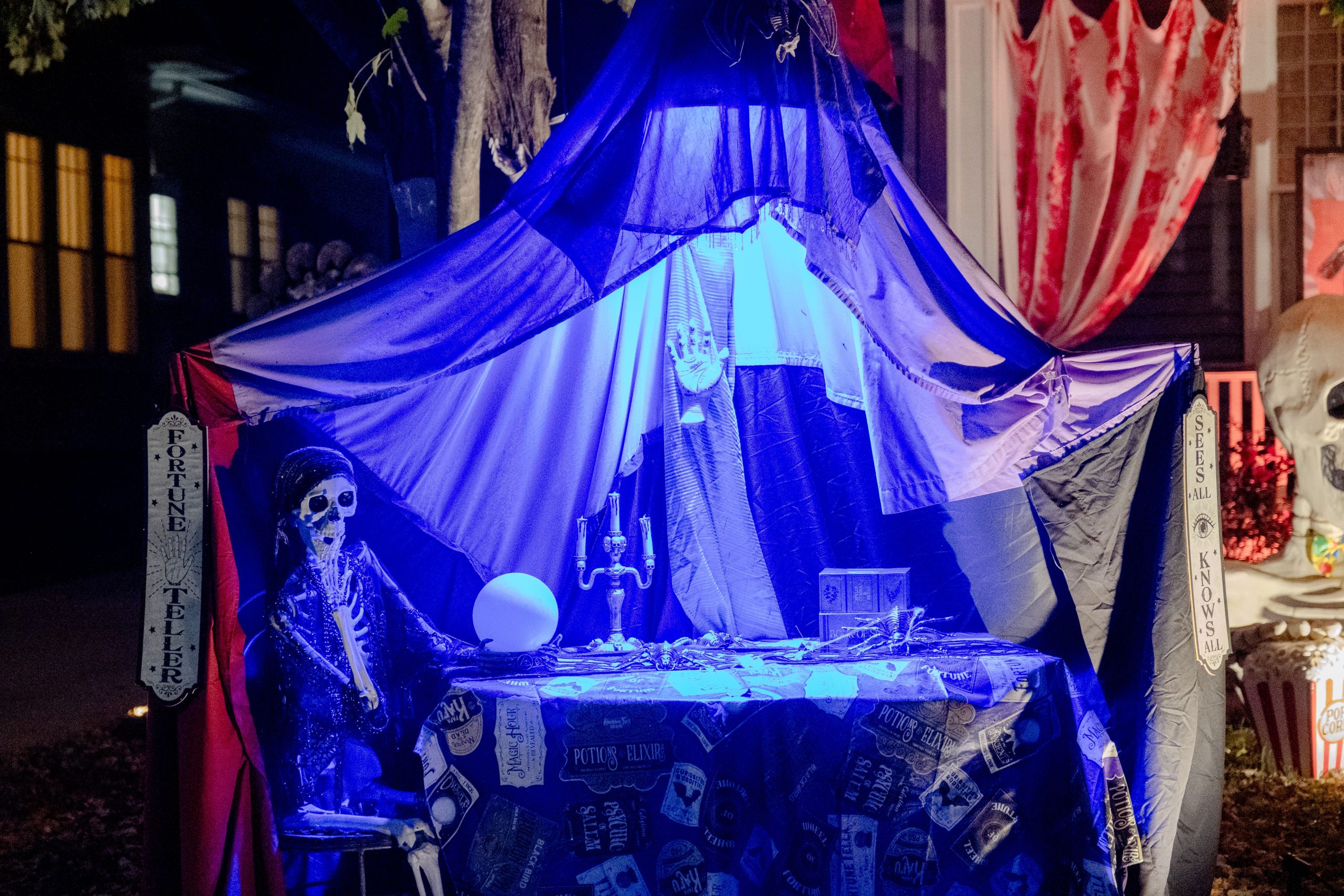 Halloween fortune teller setup with skeletons and eerie lighting outside a home.