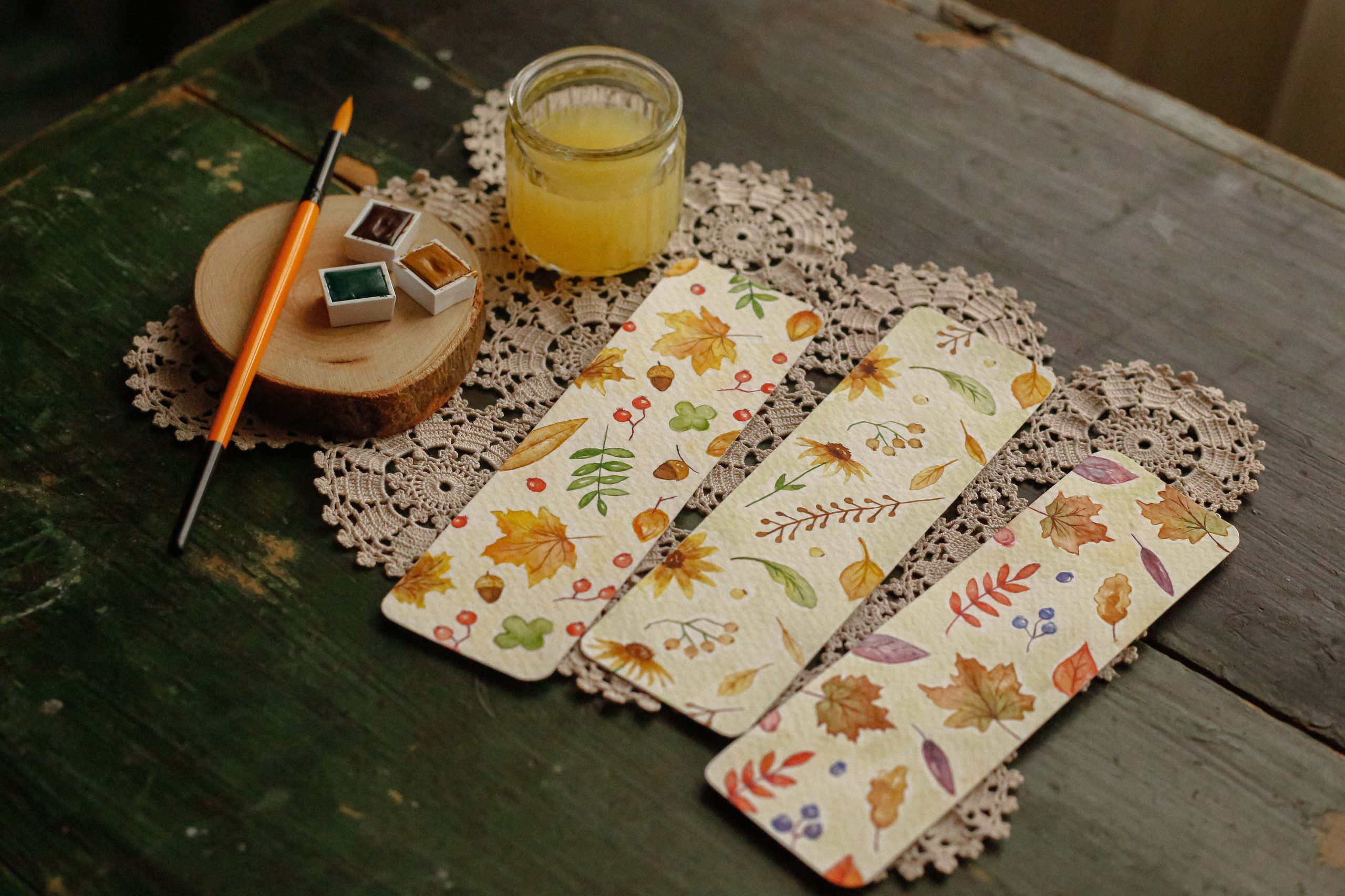 Hand-painted autumn-themed bookmarks with watercolor on a vintage table setup.