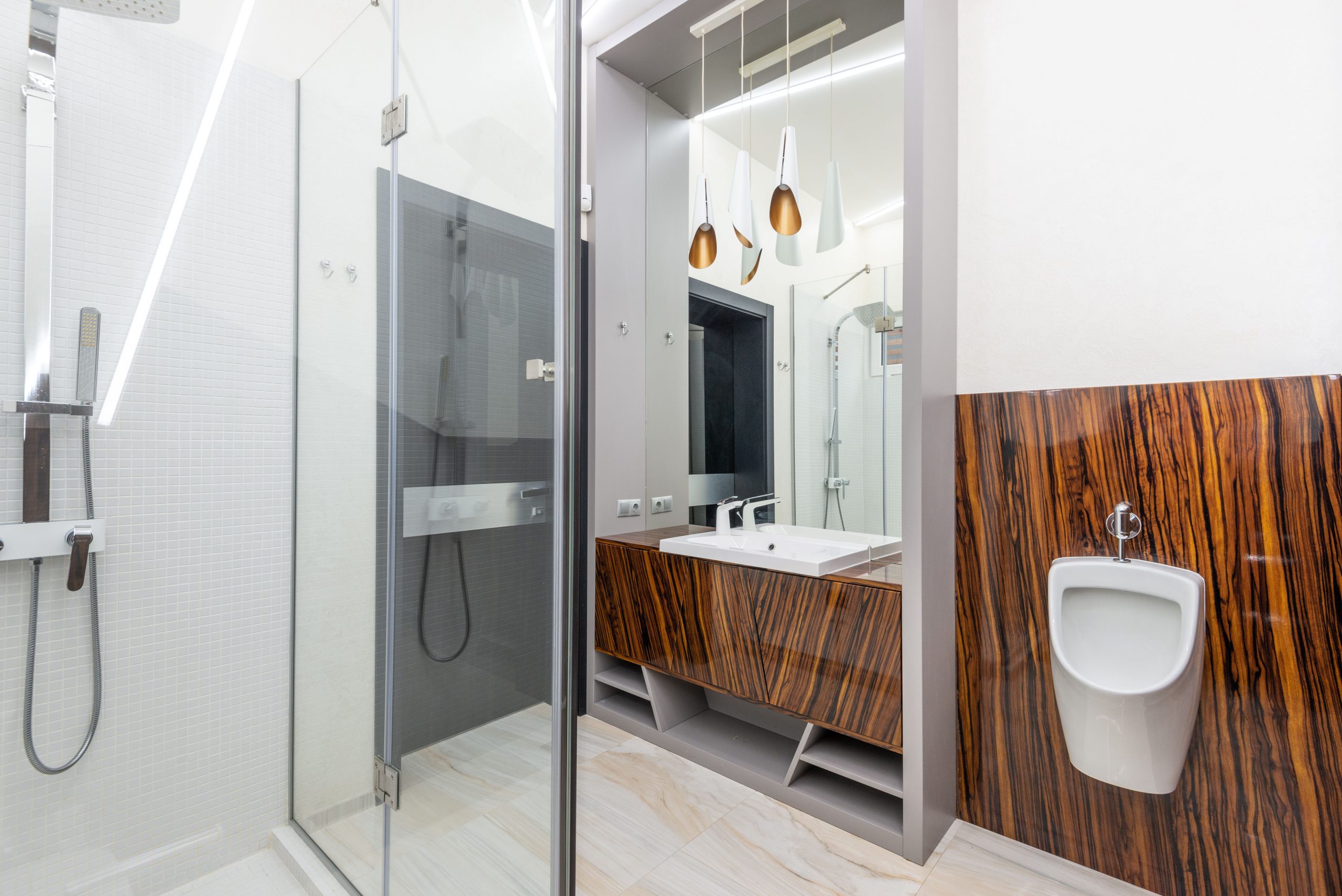 Interior of contemporary bathroom with glass shower cabin and ceramic sink and urinal
