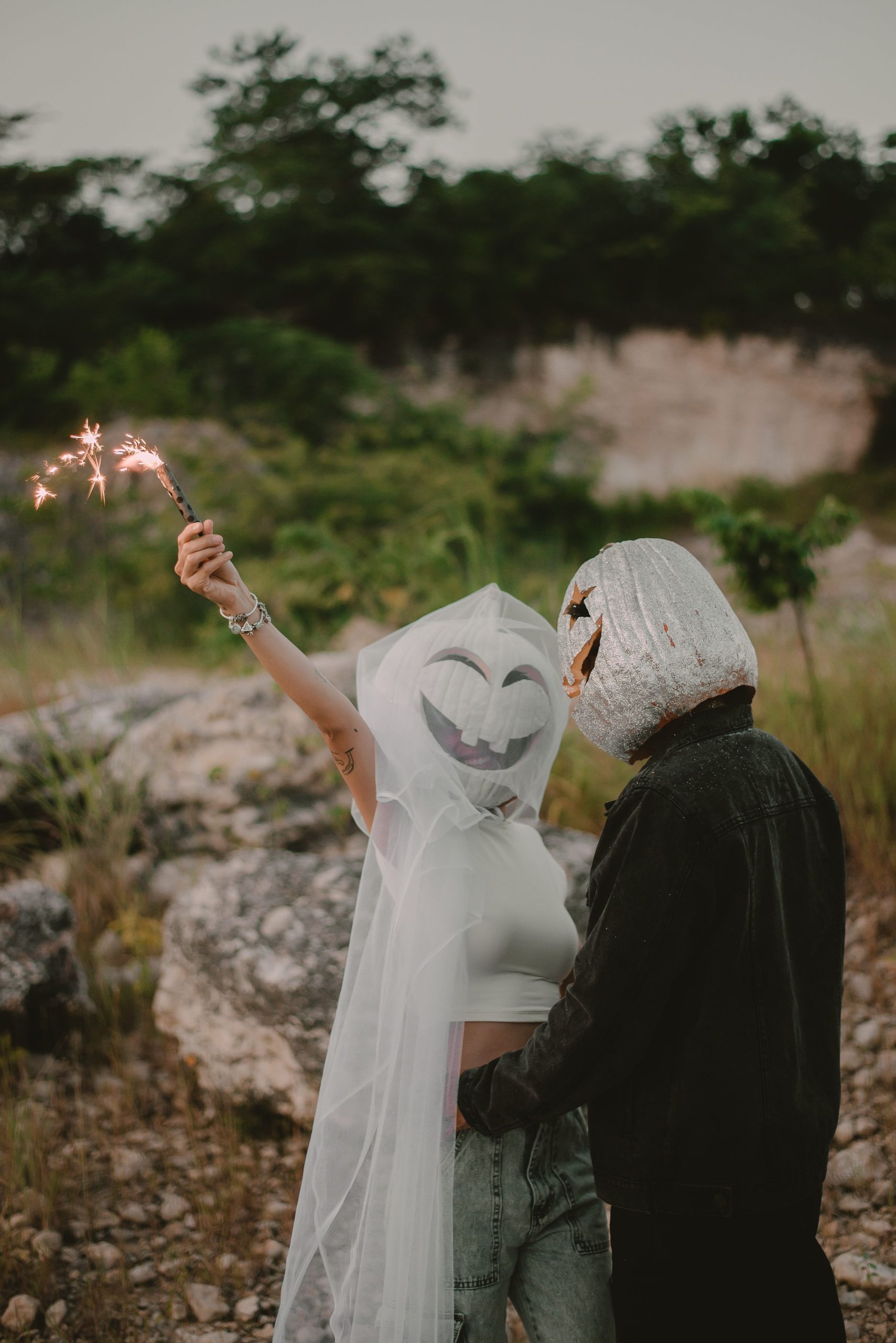 Masked couple celebrates Halloween outdoors, holding sparklers and wearing creative costumes.