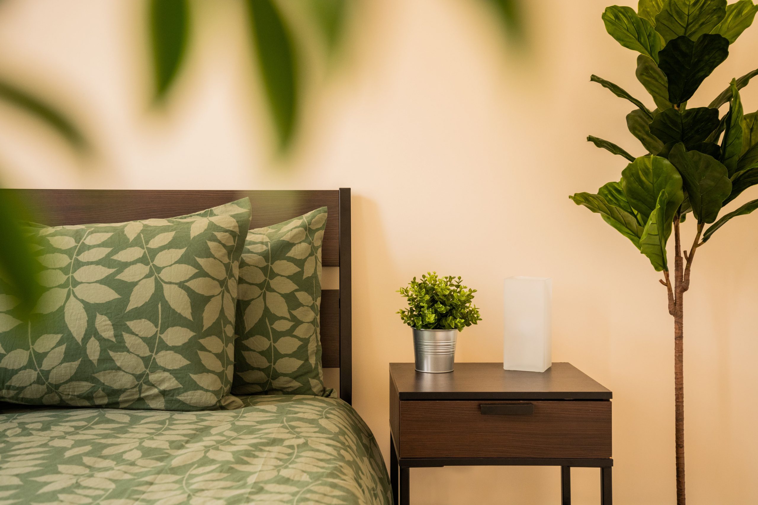 Modern bedroom featuring green leaf-patterned bedding and houseplants for a fresh nature theme.
