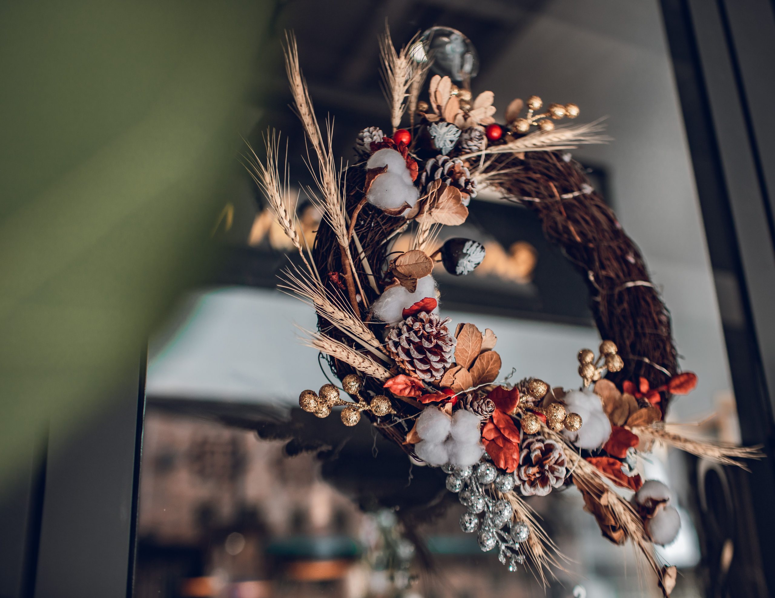 Ornate holiday wreath with pine cones and cotton on a glass door, perfect for festive decor.