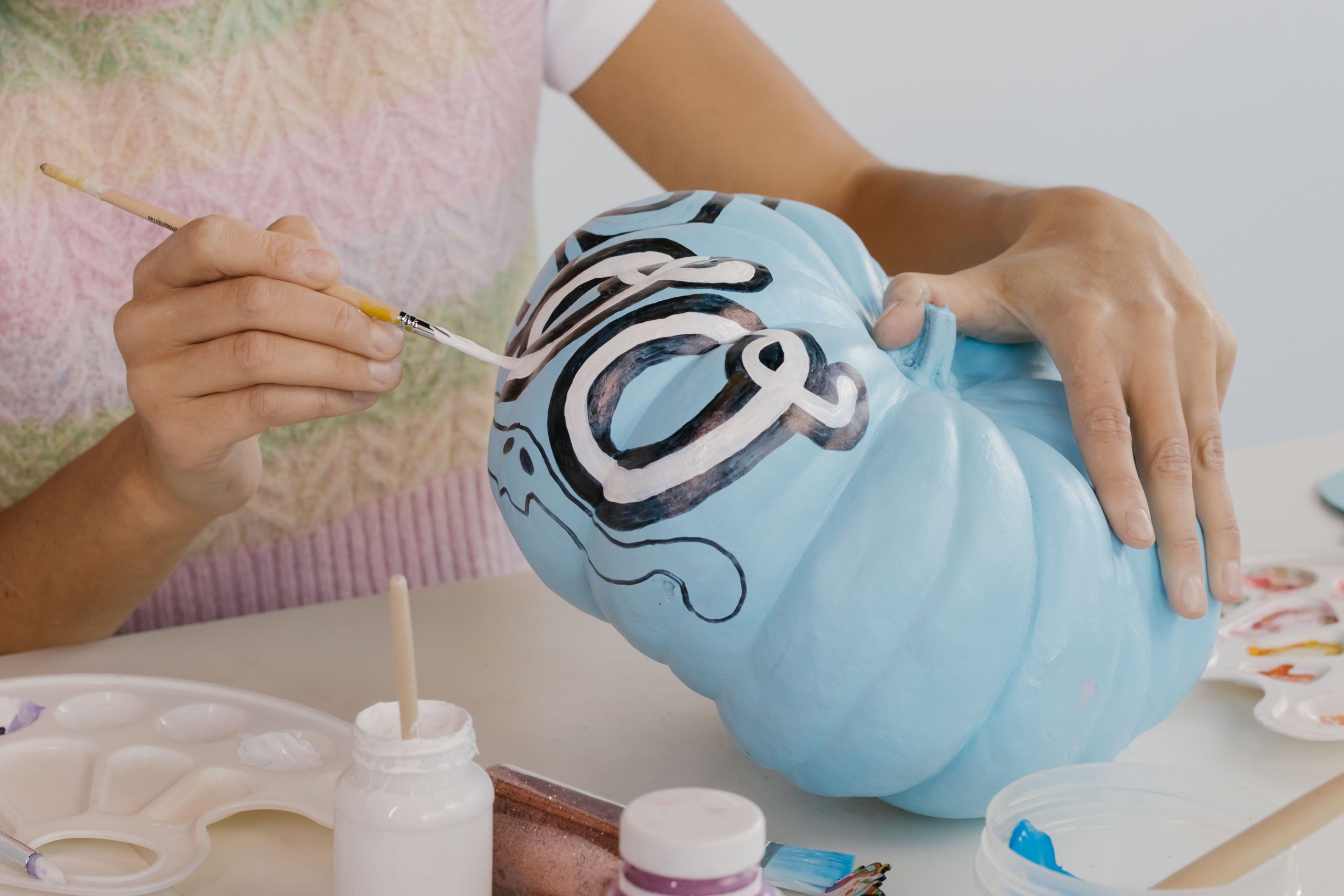 Person painting a blue pumpkin with artistic designs, perfect for fall decoration and Halloween crafts.