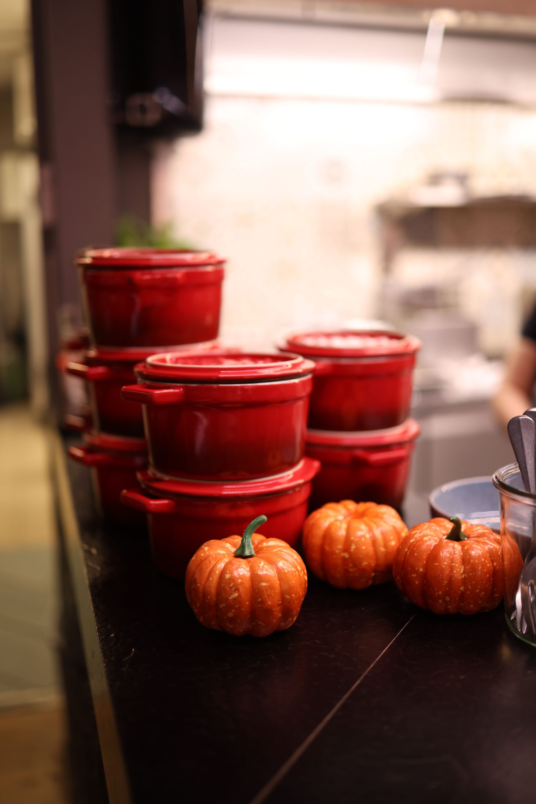 Red ceramic pots stacked on a kitchen counter with decorative pumpkins beside them.