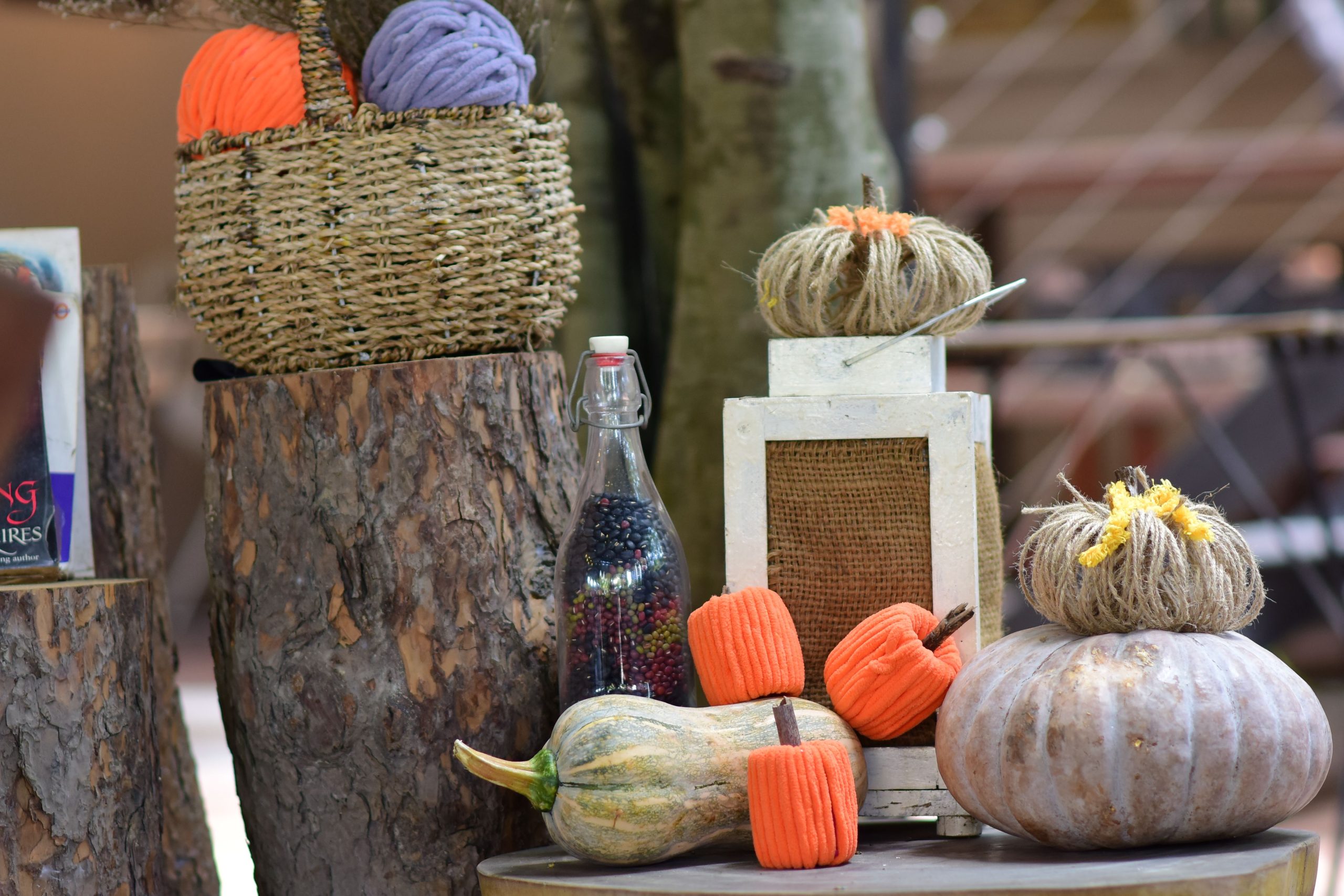 Rustic autumn decor featuring pumpkins, yarn, and wooden logs, perfect for a cozy fall ambiance.