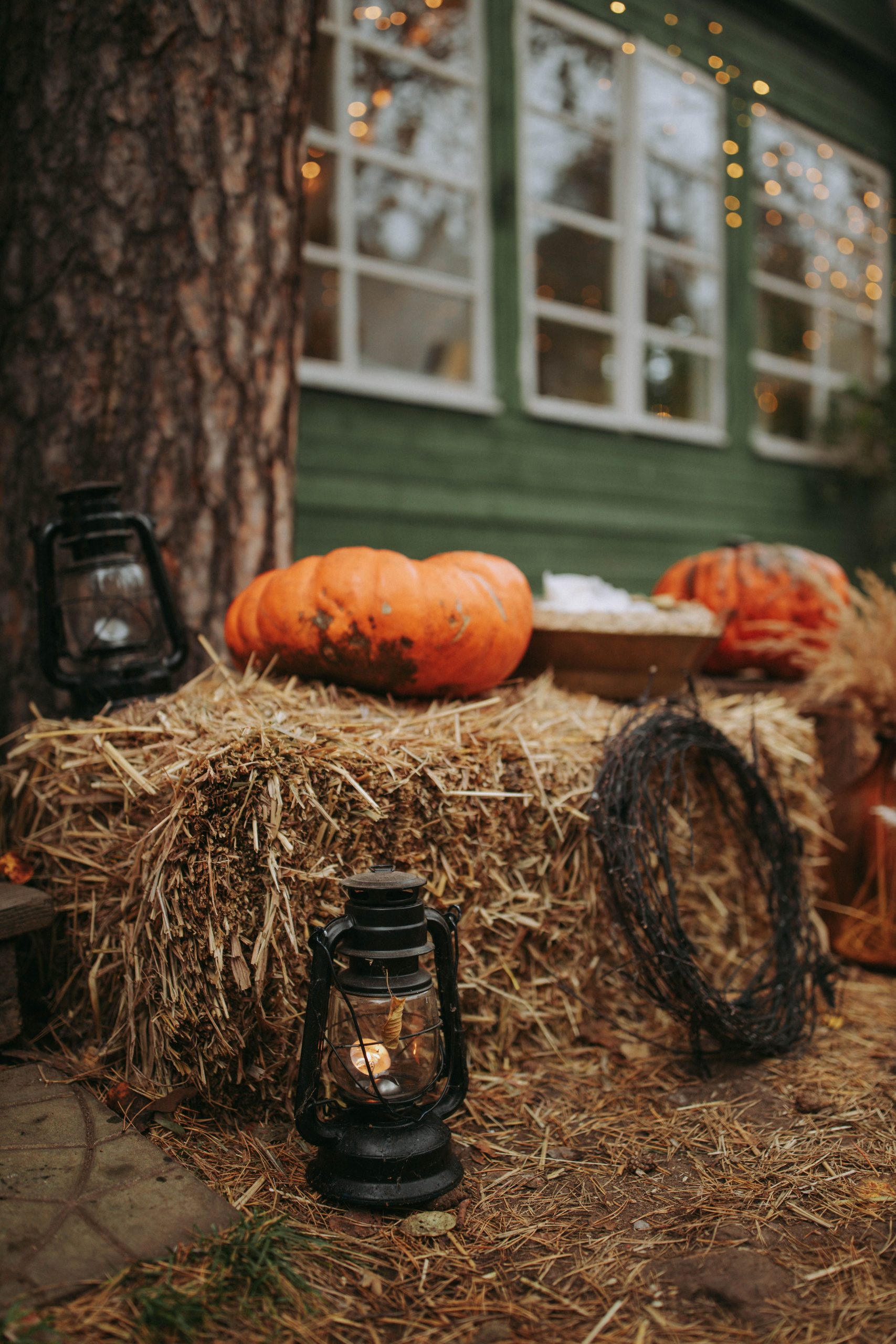Rustic autumn porch scene with pumpkins, hay bales, and lanterns, creating a festive fall atmosphere.