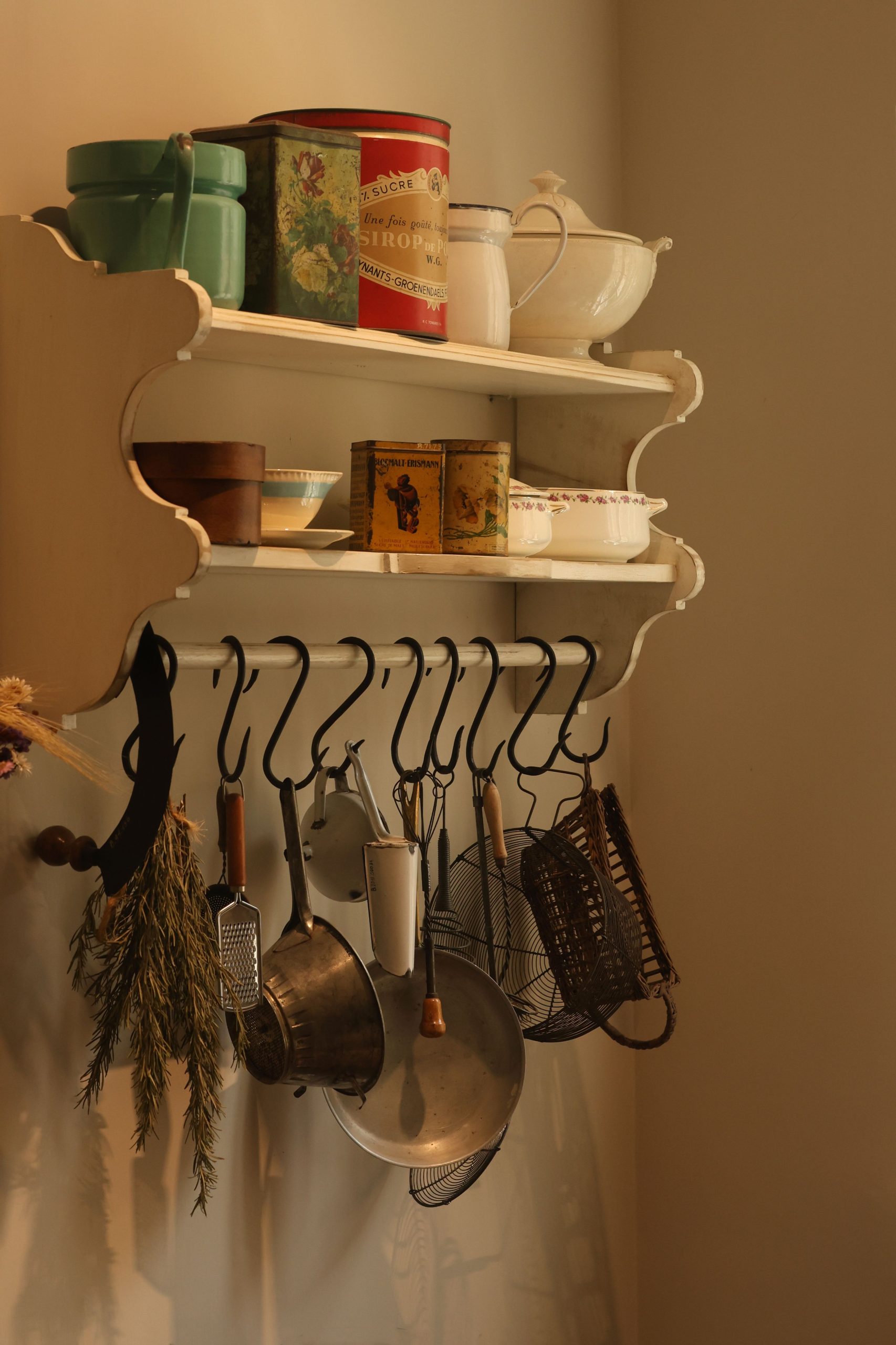 Rustic kitchen shelf with vintage tins and hanging cookware, warm tones.