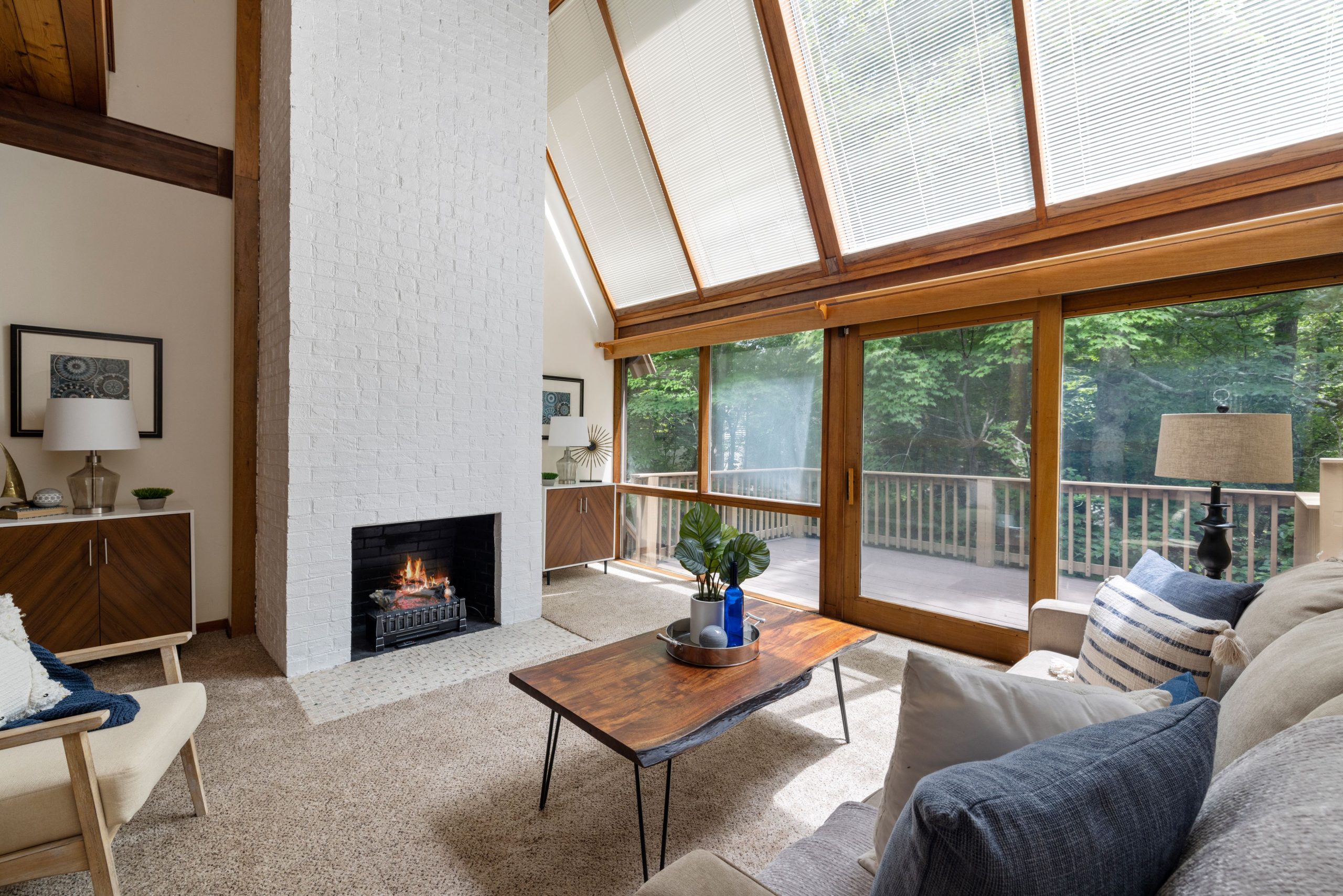 Spacious living room featuring a cozy fireplace and large windows overlooking forest greenery.