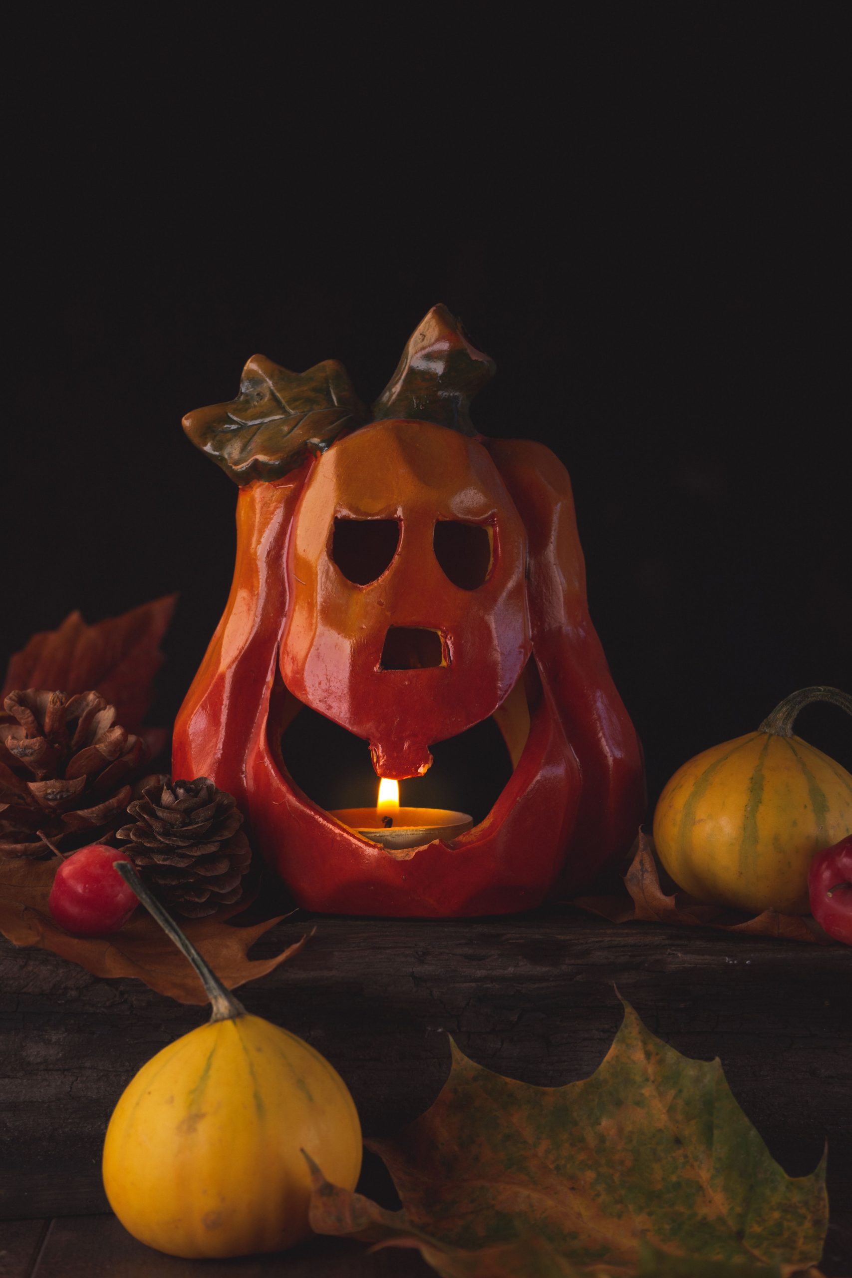 Spooky Halloween scene with a candlelit pumpkin, pine cones, and fall leaves.