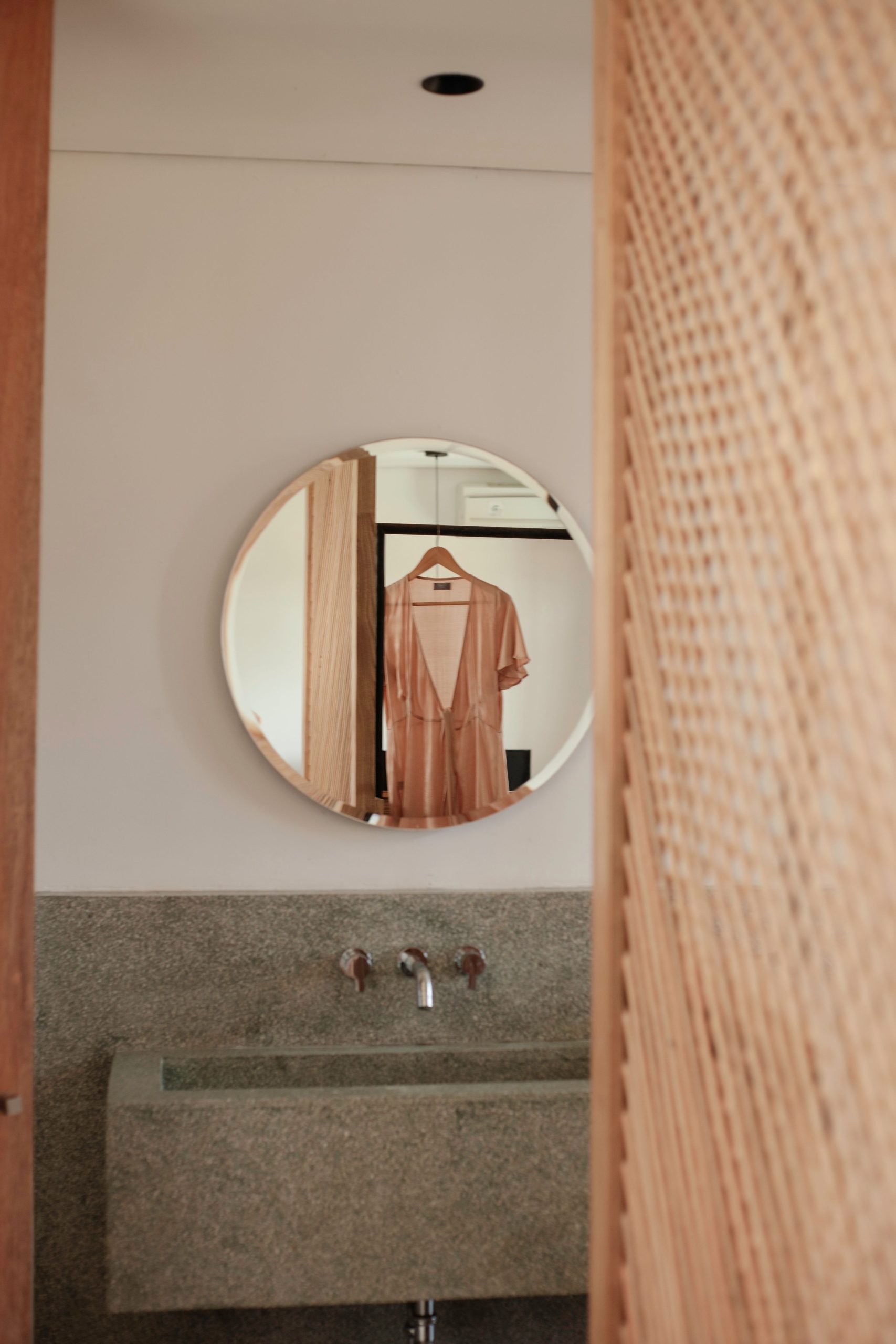 Stylish dress hangs reflected in a round mirror, enhancing a modern bathroom's minimalist decor.